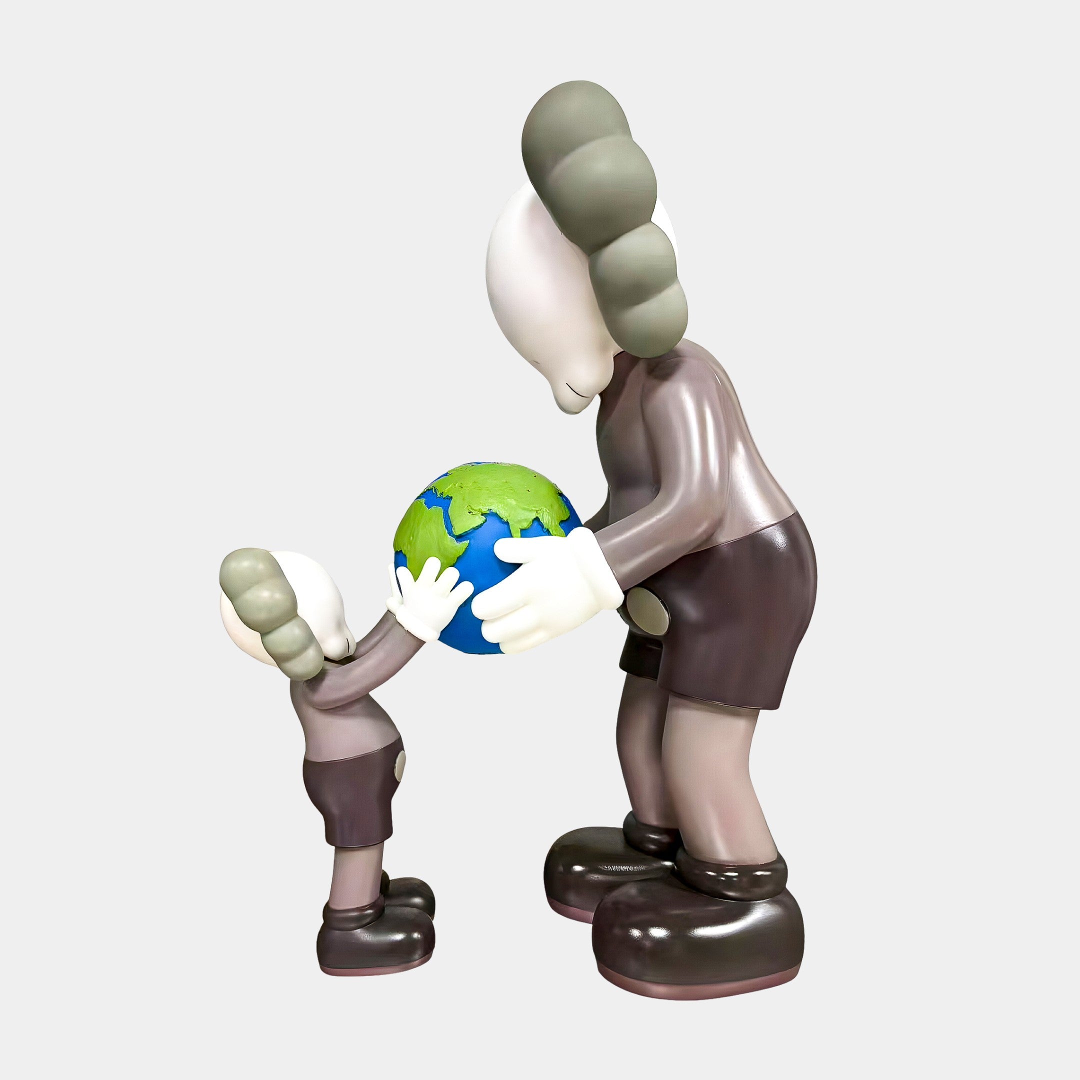 The Giant Sculptures Hazelnut Brown Iconify Atlas Figure (30cm) features two cartoon-like characters, one tall and one small with gray hair, holding a globe—an ideal symbolic sculpture for sharing or teaching about the world in your home office.
