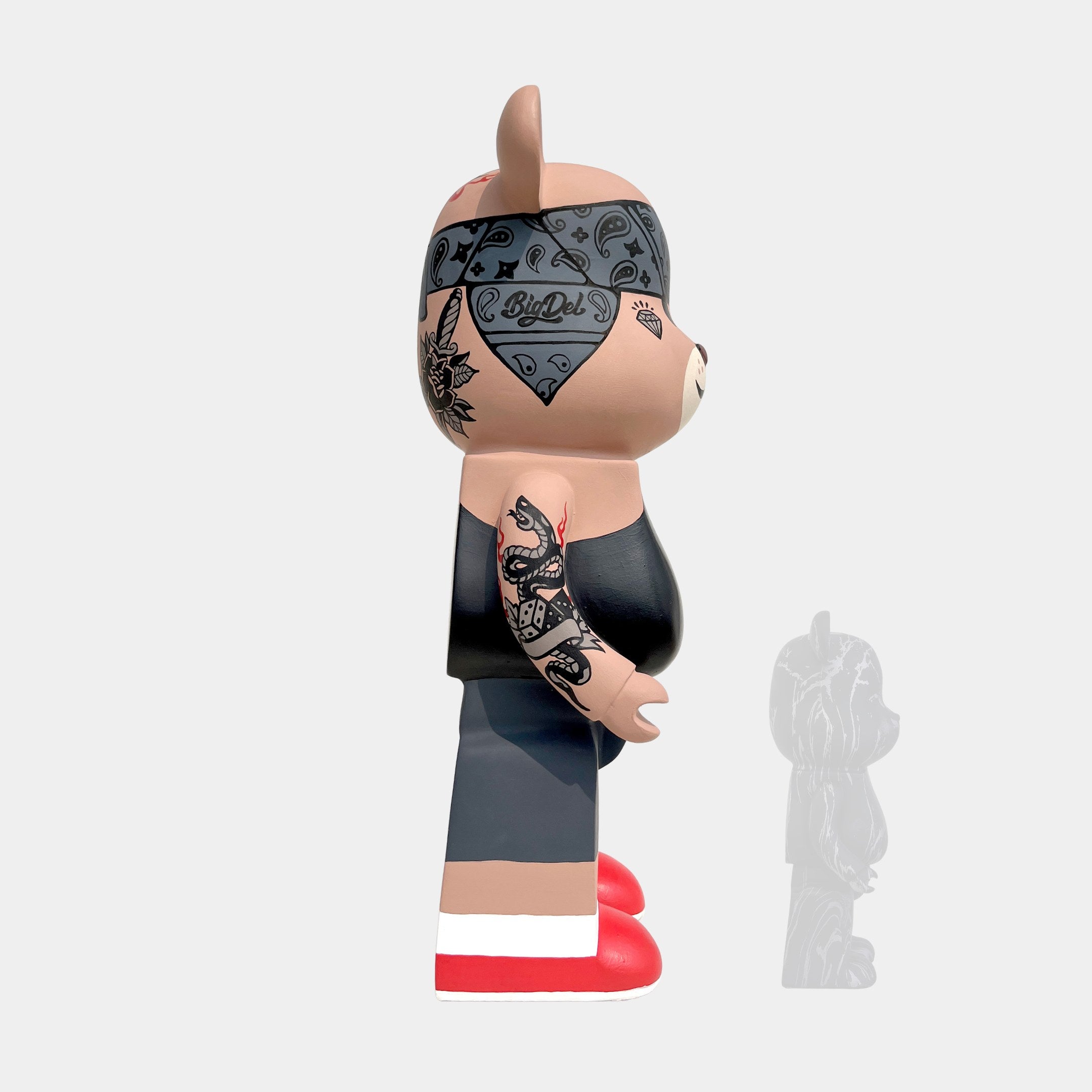 The Iron Paw Bear Sculpture - 50cm by Giant Sculptures is a limited edition vinyl bear with tattoos, wearing a black tank top, dark pants, and red shoes, shown in profile on a light background with its faint shadow.