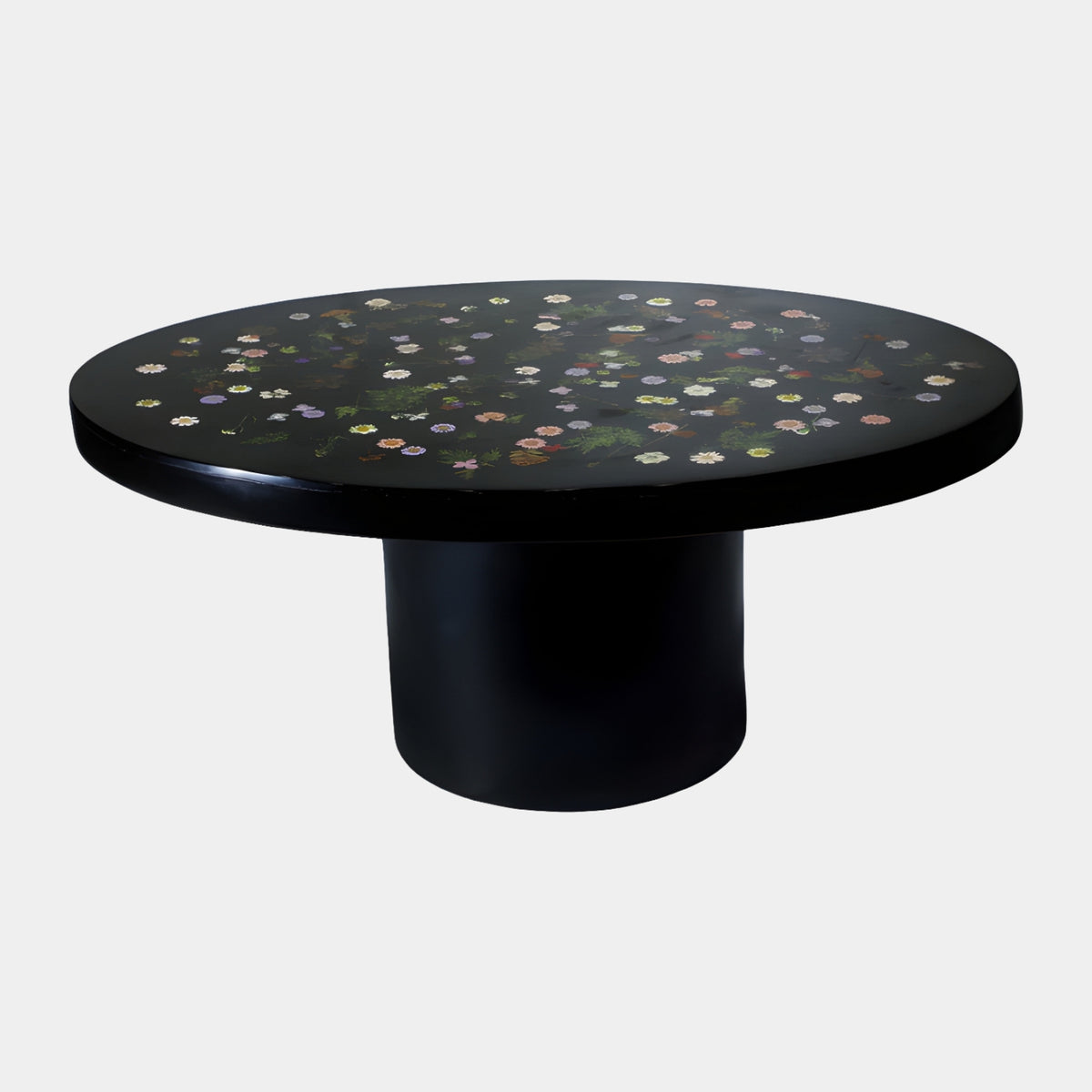 Black Flowerhead Resin Coffee Table - 100cm with an oval glazed black top scattered with white, pink, violet, yellow and orange flowerheads and fern foliage, set on a cylindrical black pedestal base against a plain light grey background.