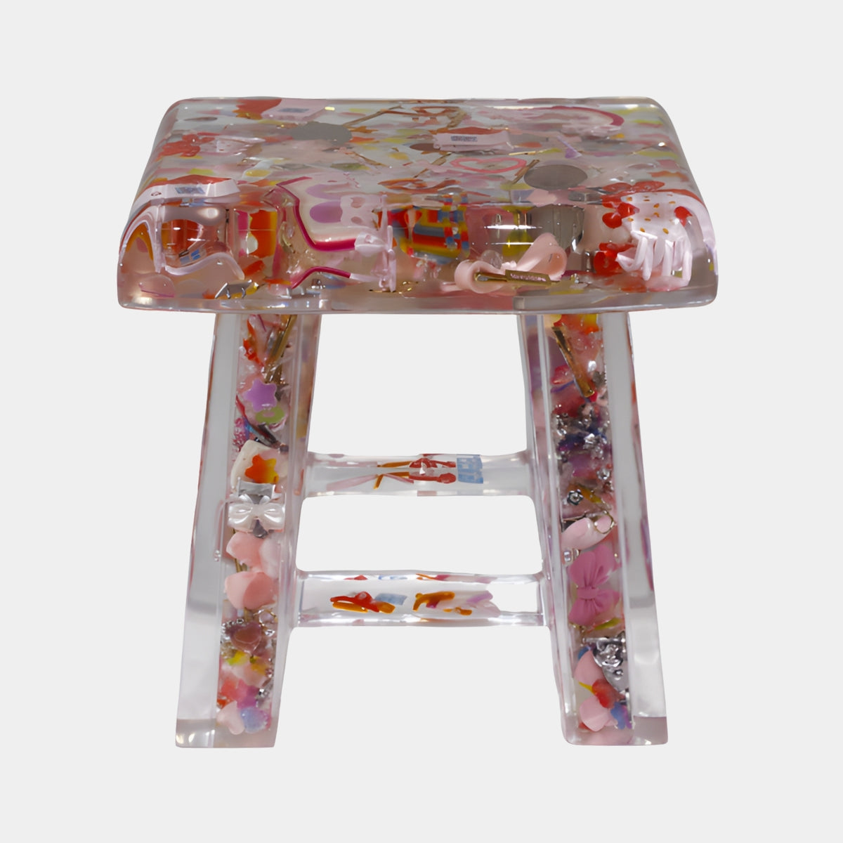 Clear Set Object Cast Resin Stool (30cm) by Giant Sculptures, four-legged design embedding pink, red and yellow small objects, shown against a plain white background.