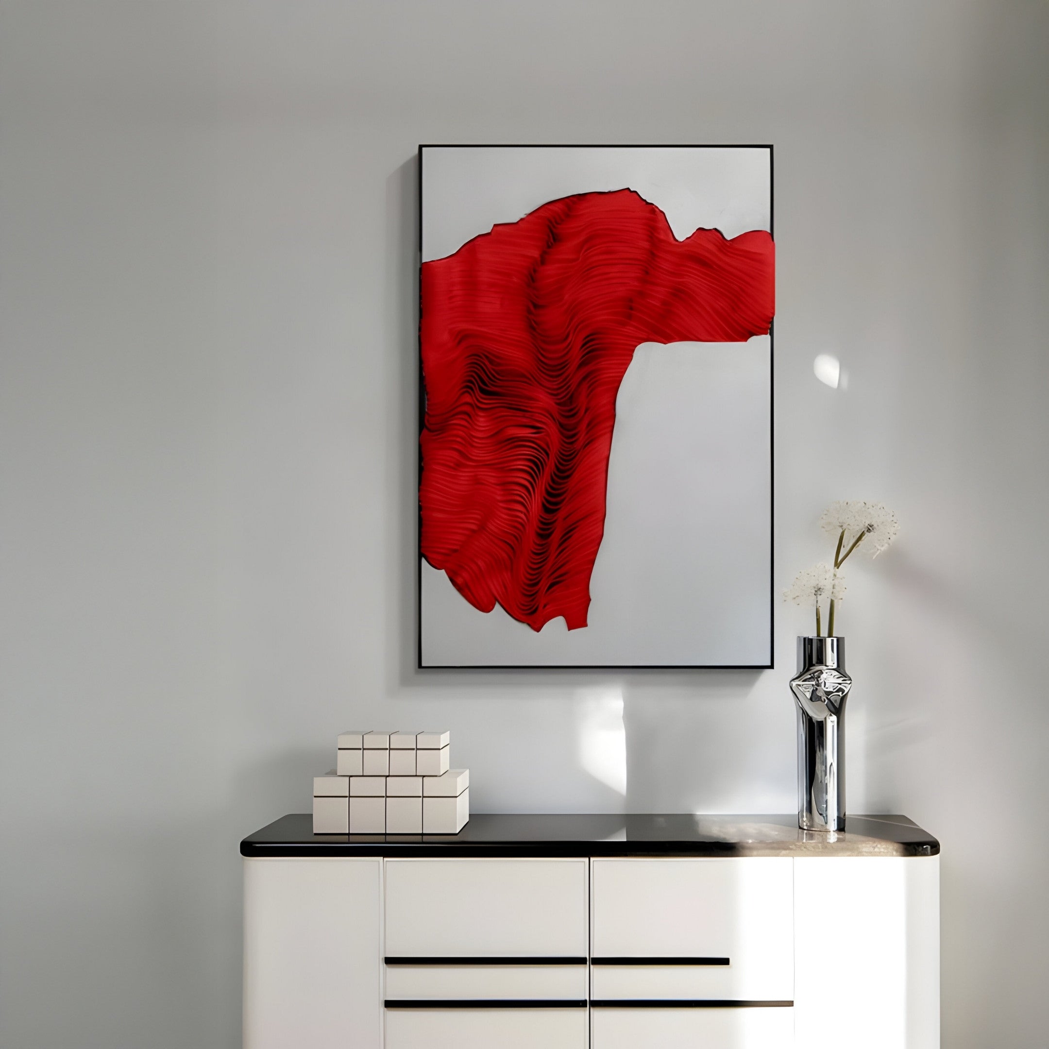 A modern interior features a white cabinet with books and a vase of white flowers, while above, Giant Sculptures’ Ravelle Red Contour Felt 3D Relief Wall Art creates a bold focal point on the light gray wall.