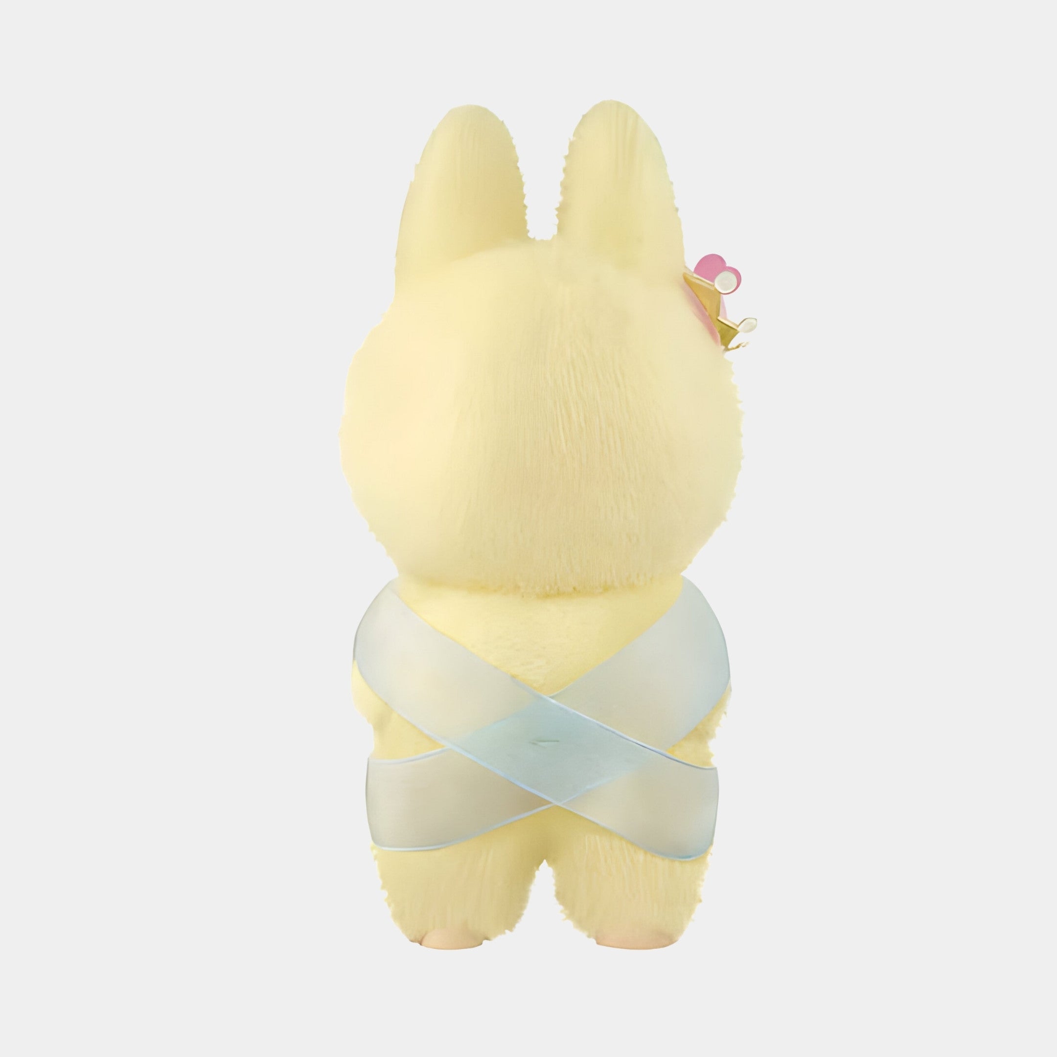 A plush yellow bunny with a shiny blue ribbon and gold crown with pink heart on its ear faces away against a light gray background. This scene captures the charm of The Monster Lets Checkmate Heart Labubu Sculpture - 160cm by Giant Sculptures.