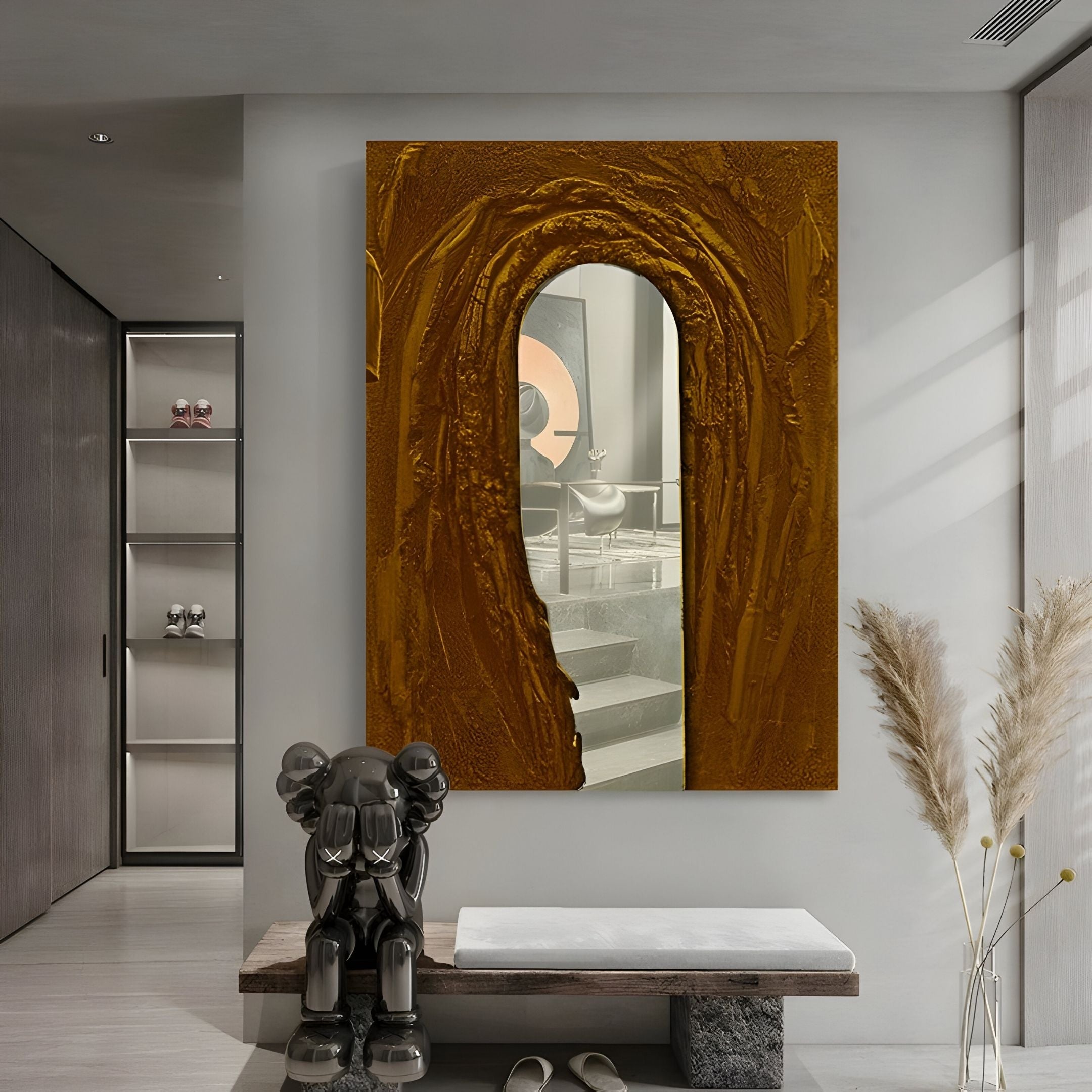 A modern hallway features the Arclunor Bronze Arch Relief Mirror 3D Wall Art by Giant Sculptures, a black abstract sculpture on a bench, tall pampas grass in a vase, shelves, and additional 3D wall art for added depth and interest.