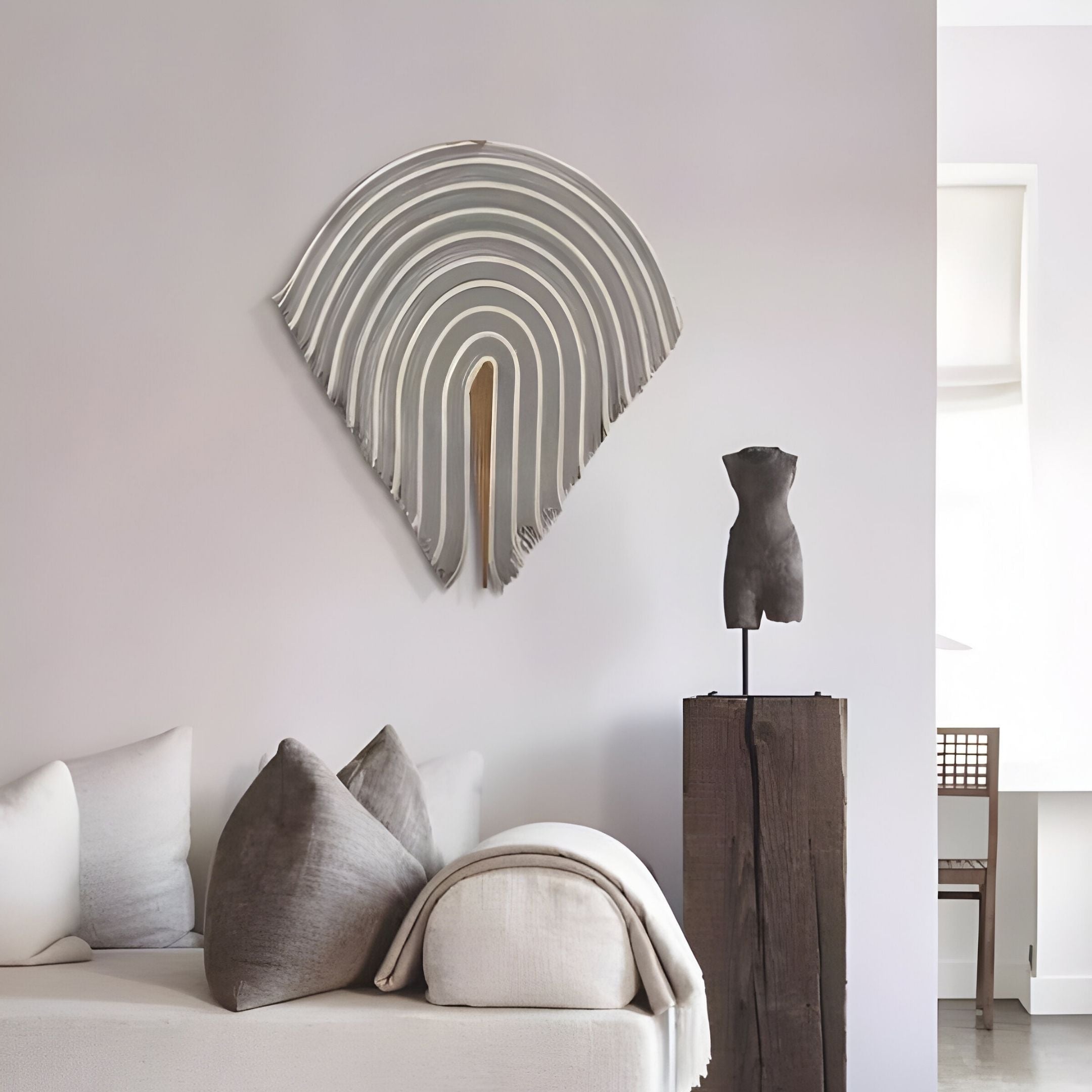 Minimalist living room with a white sofa and neutral pillows, featuring Arclune Grey & White Stripe Sculptural Felt 3D Wall Art by Giant Sculptures above the couch. A small black torso sculpture on a wooden pedestal adds wabi-sabi charm.