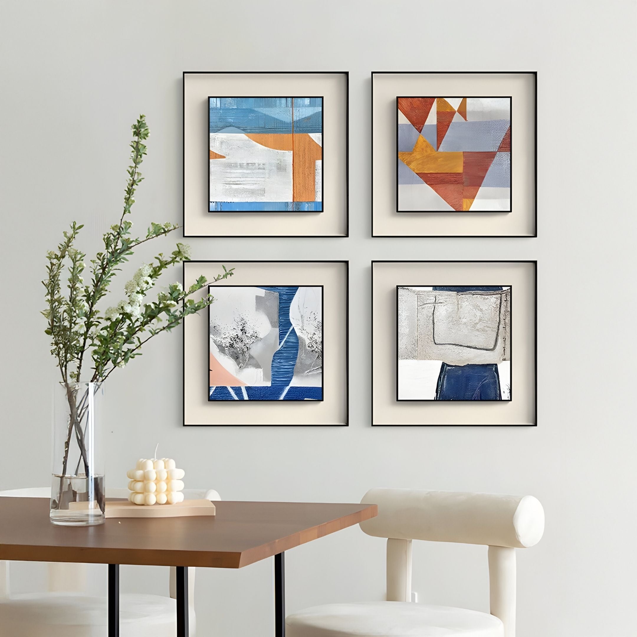 A modern dining area features a wooden table, two white upholstered chairs, a vase with green branches, a candle, and four Giant Sculptures Aerolith Blue Cascade Abstract Textured Framed Wall Art pieces on a light-colored wall.