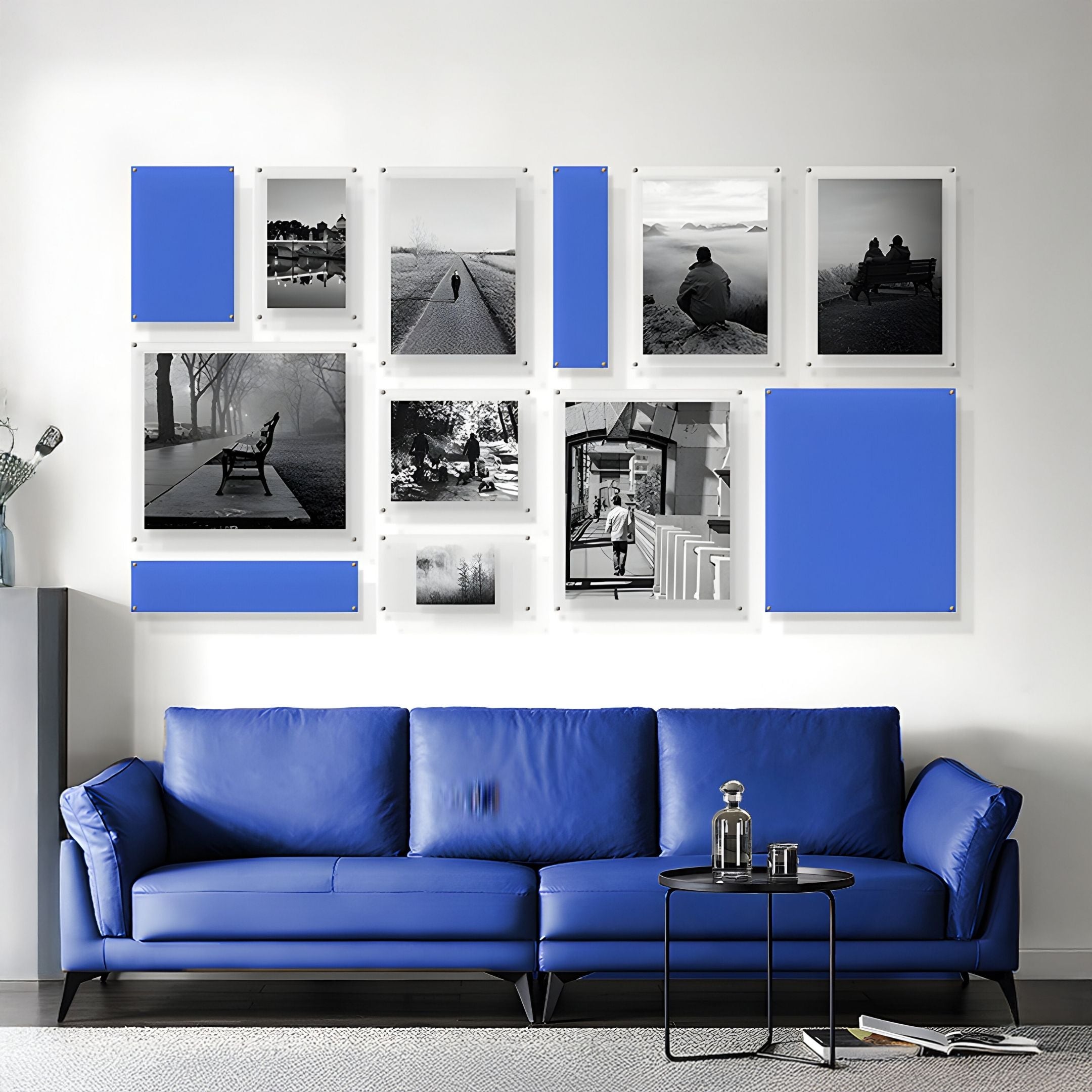 A modern living room features a blue sofa, round black coffee table, and the Framegrid Blue Mixed-Size Gallery 12-Set Acrylic Wall Art by Giant Sculptures—an ideal grid of blue and black-and-white pieces for contemporary interiors.