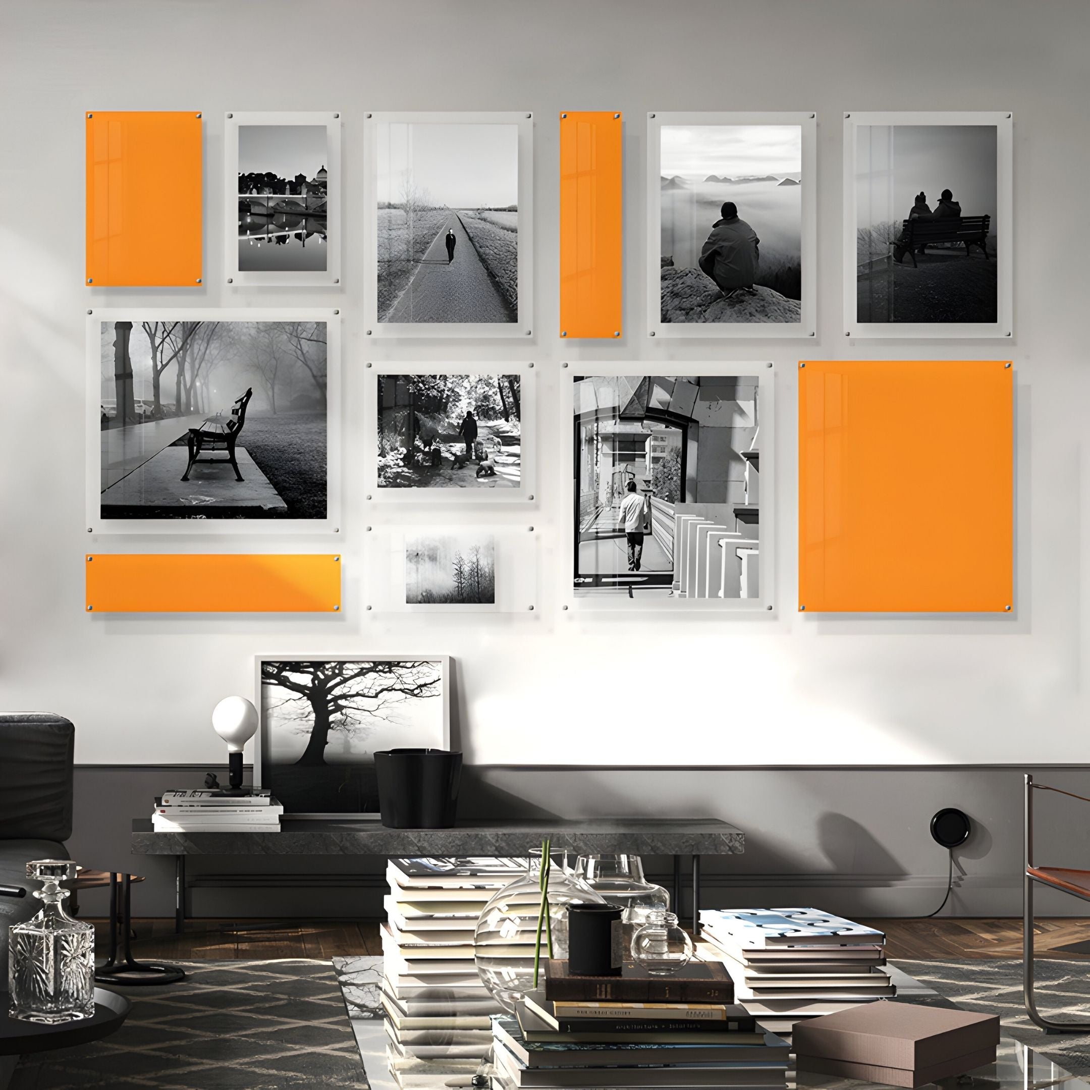 A modern living room features the Giant Sculptures Framegrid Orange Mixed-Size Gallery 12-Set Acrylic Wall Art, combining black-and-white photos and orange panels above a sleek console with books, decor, and a tree photo on top.