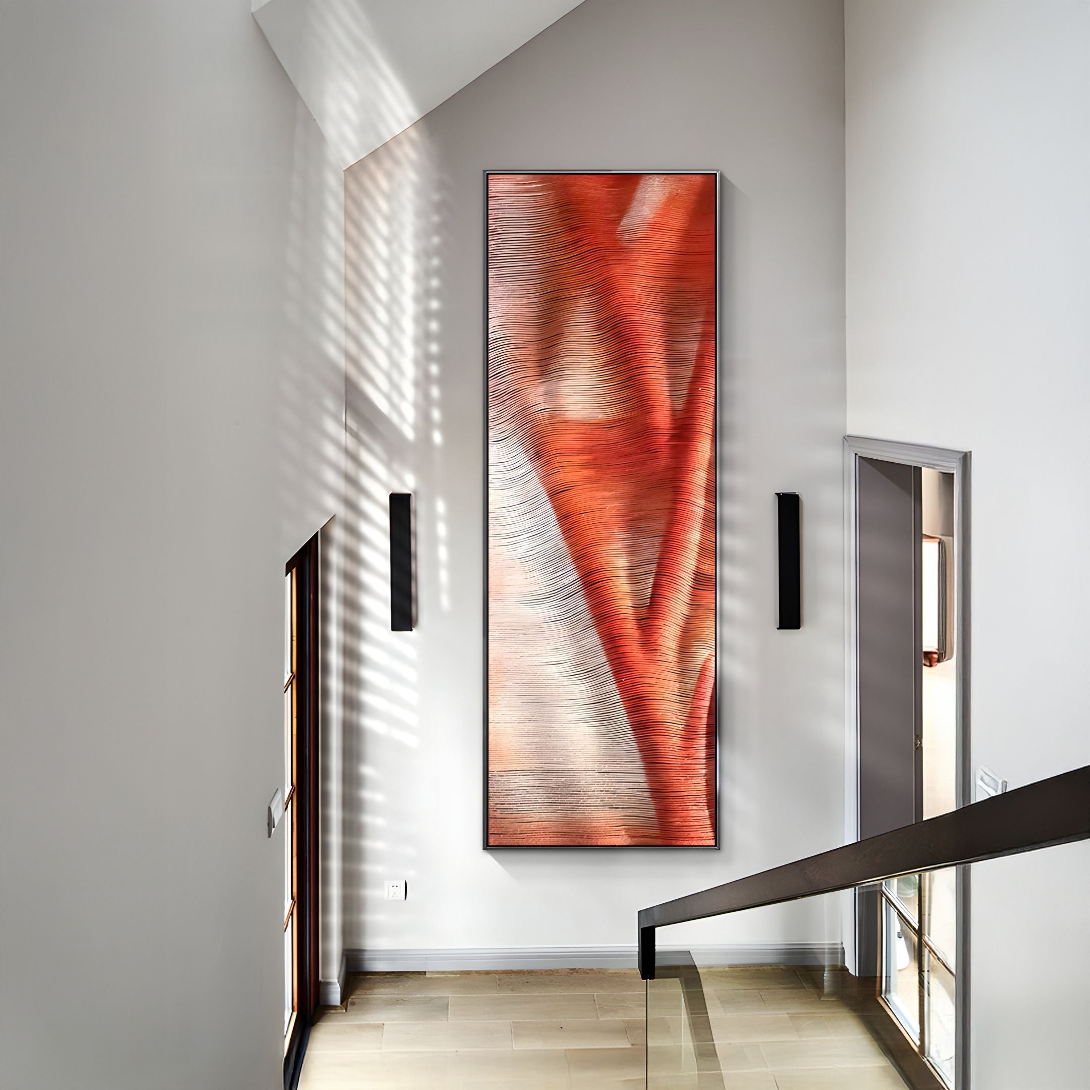 A modern hallway features the Rivara Ember Wave Vertical Hand-Painted Rope 3D Wall Art by Giant Sculptures in bold red and orange hues on a white wall, framed by black sconces as sunlight casts dramatic shadows across the space.