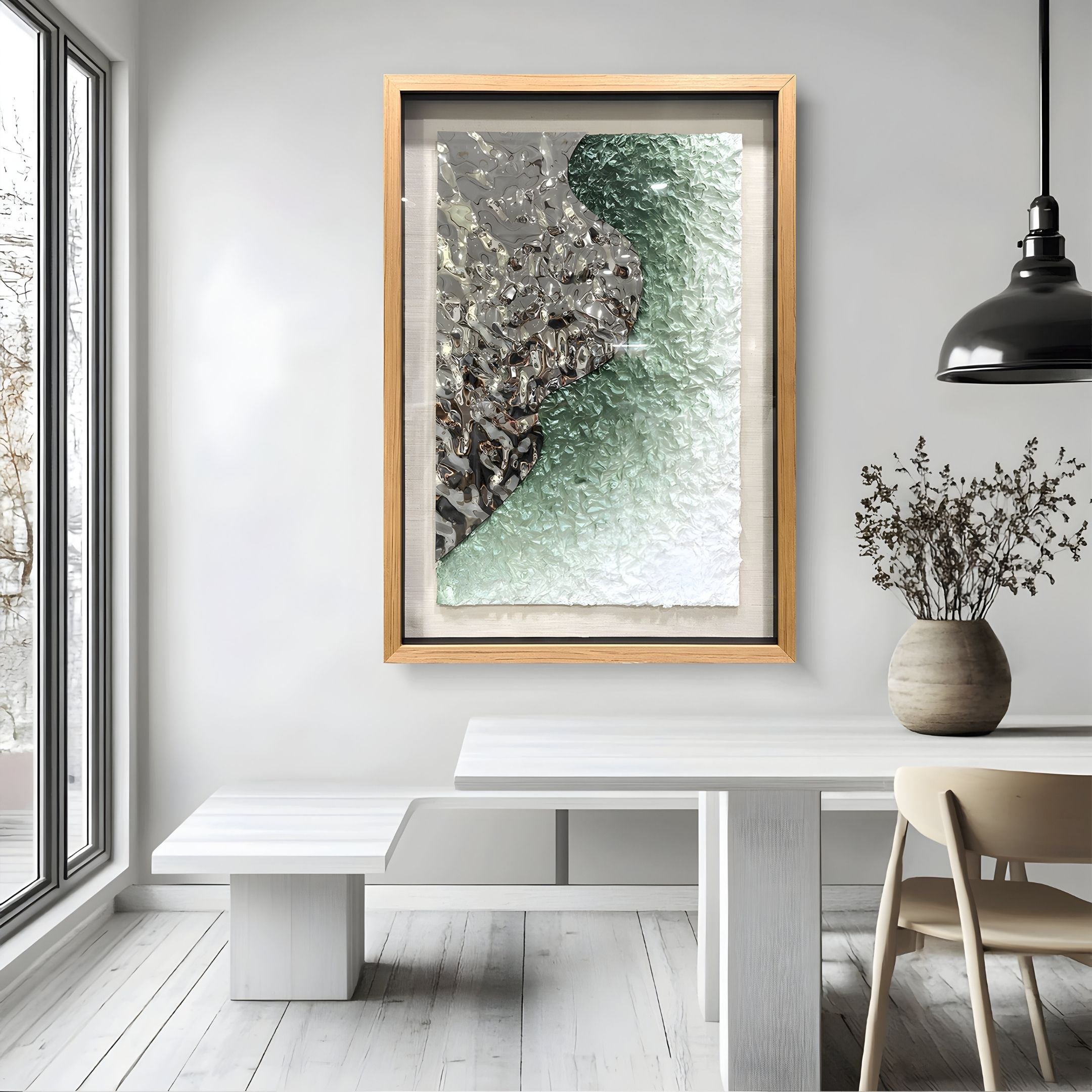 A modern dining room features a white table, bench, beige chair, black pendant light, and the Aurivell I Silver & Green Textured Metal 3D Wall Art by Giant Sculptures. A vase with dried branches adds an organic touch to the space.