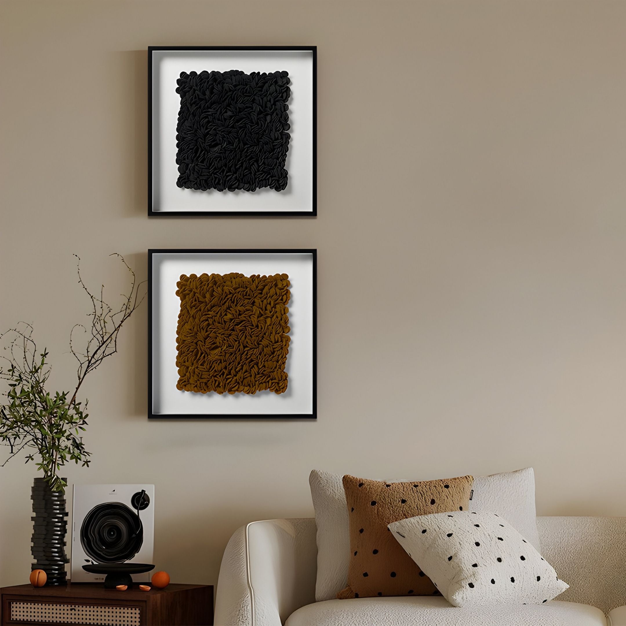 A modern living room with beige walls, a Petalus Brown Ochre Layered Felt 3D Wall Art by Giant Sculptures, black and brown abstract framed art, a white sofa with polka dot pillows, a black speaker, vase with branches, and minimal decor on a wooden table.