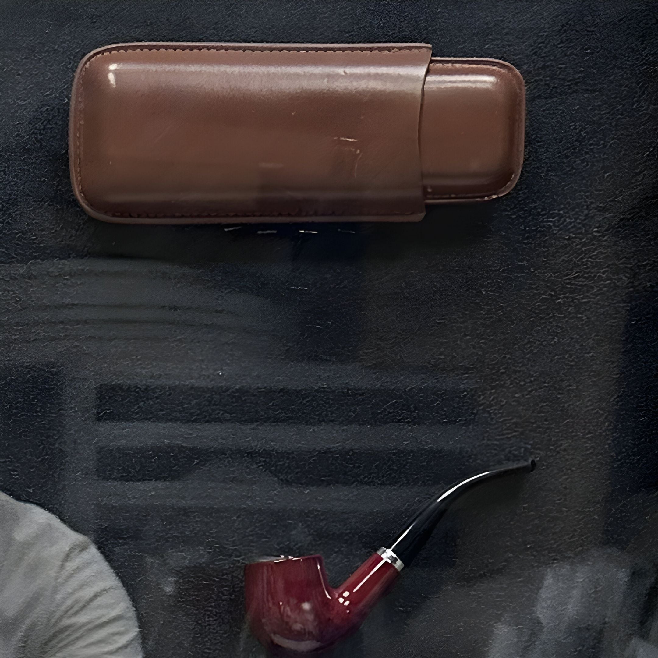 The Vintor Gentleman Pipe, Cigar & Heritage Framed Wall Art by Giant Sculptures features a brown leather case above a red and black curved pipe on a dark surface, with a person's shoulder visible, evoking vintage-inspired style.