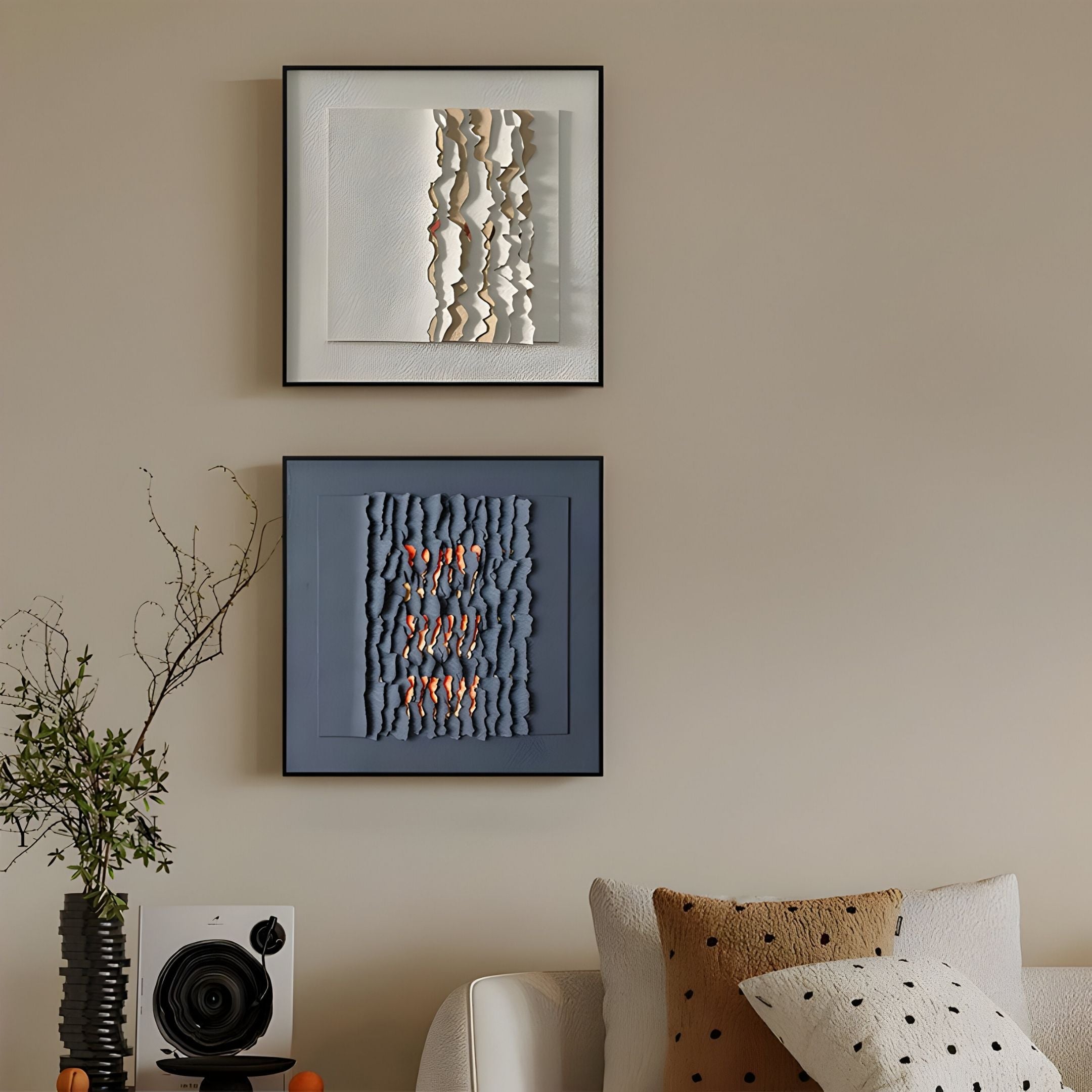 Two Rivura Navy Layered Sandstone Texture 3D Wall Art pieces by Giant Sculptures hang above a white sofa with patterned pillows. A small speaker and a vase with branches on the side table complete the modern, cozy decor.