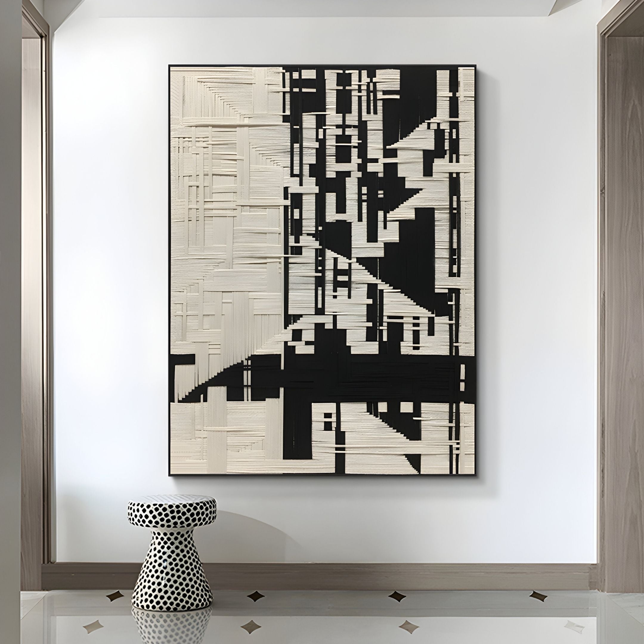 The Lintrix Black & White Geometric Woollen Knit 3D Wall Art by Giant Sculptures hangs above a black-and-white polka dot stool in a modern room with wood door frames and tiled floors.