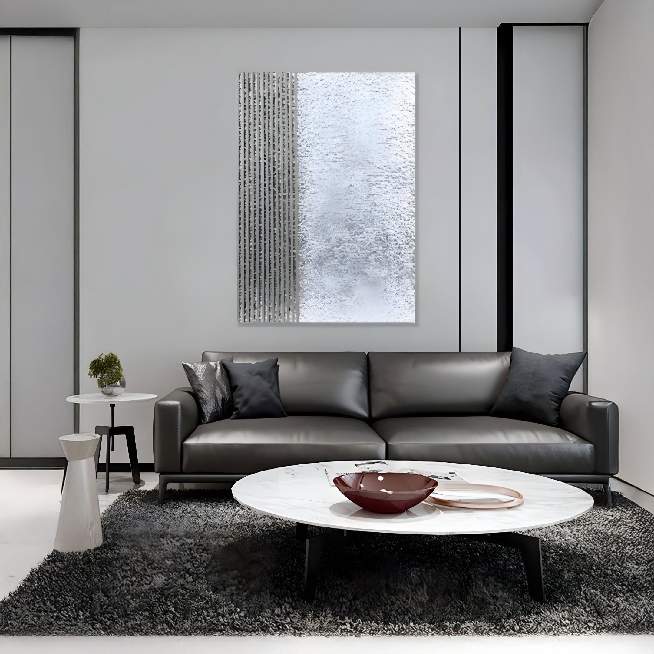 A modern living room features a gray sofa, black and gray pillows, a round white marble coffee table, decorative bowls, a gray rug, and the Metallure Silver Linear Textured Acrylic Silver Foil 3D Wall Art by Giant Sculptures on a light gray wall.