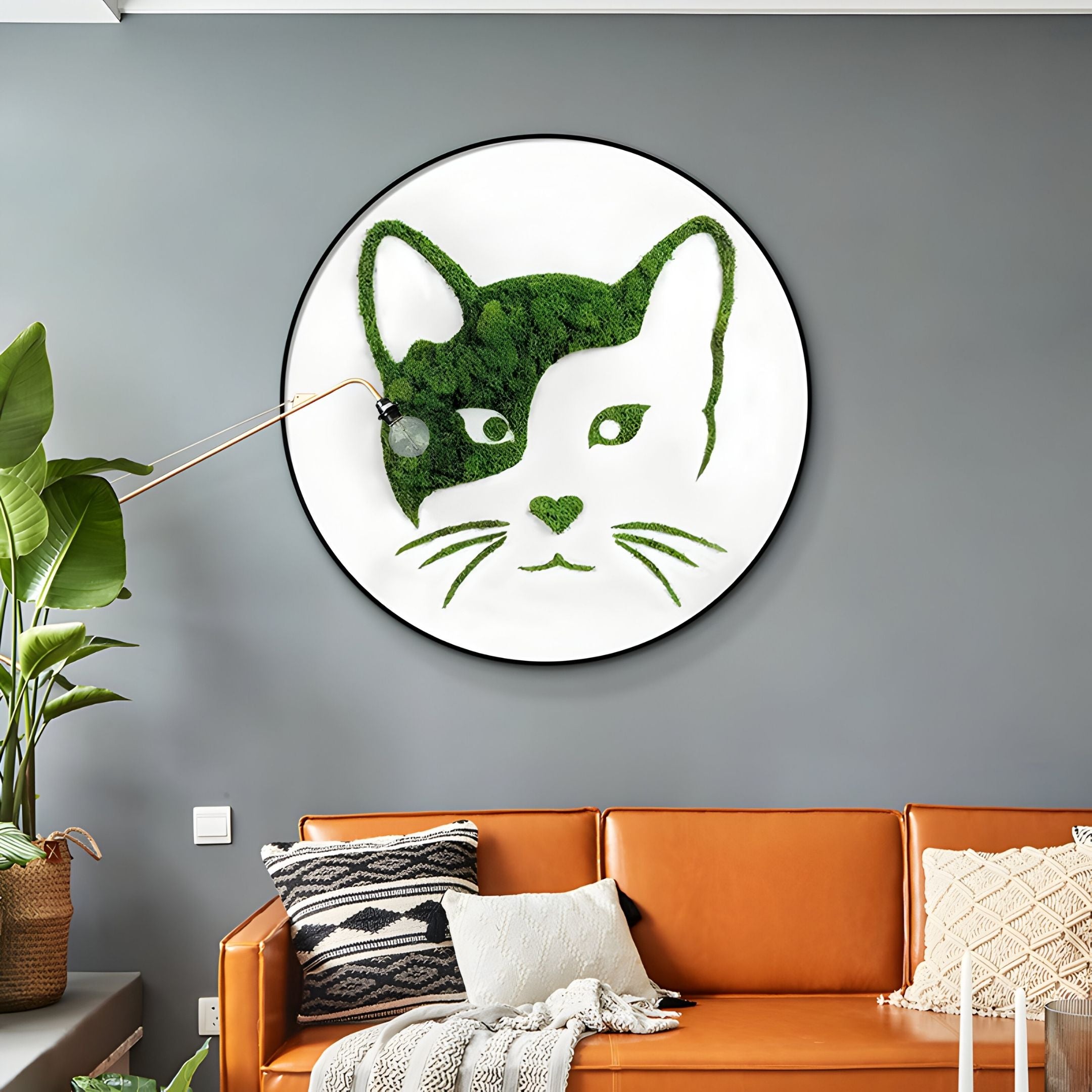 A modern living room showcases the Verdifable Round Green Cat Portrait Moss 3D Wall Art by Giant Sculptures, a brown leather sofa with patterned cushions, and a tall green plant for a touch of Scandinavian decor.