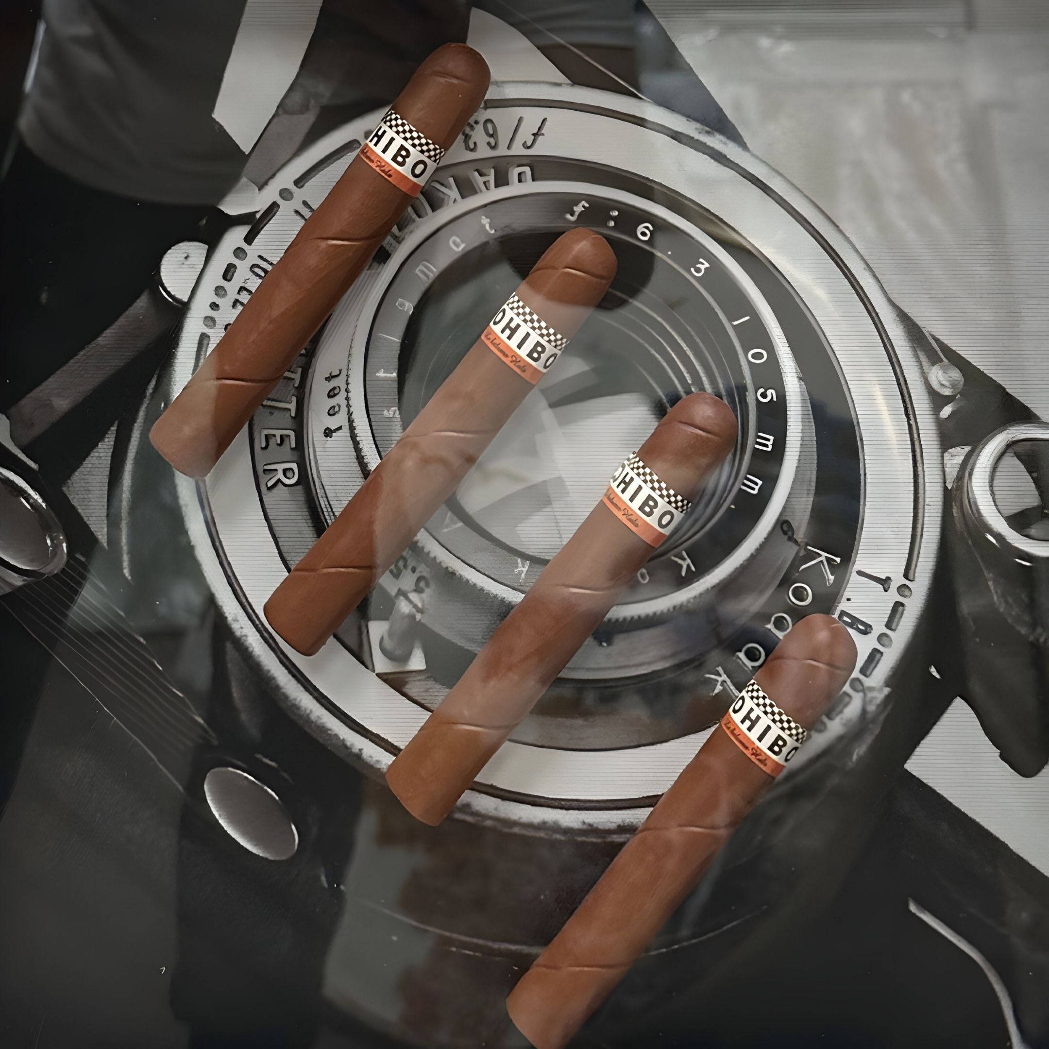 The Prestivo Cigar & Vintage Camera Framed Display Wall Art by Giant Sculptures features four brown cigars resting on a black-and-white vintage camera lens, creating a striking and unique decor piece.