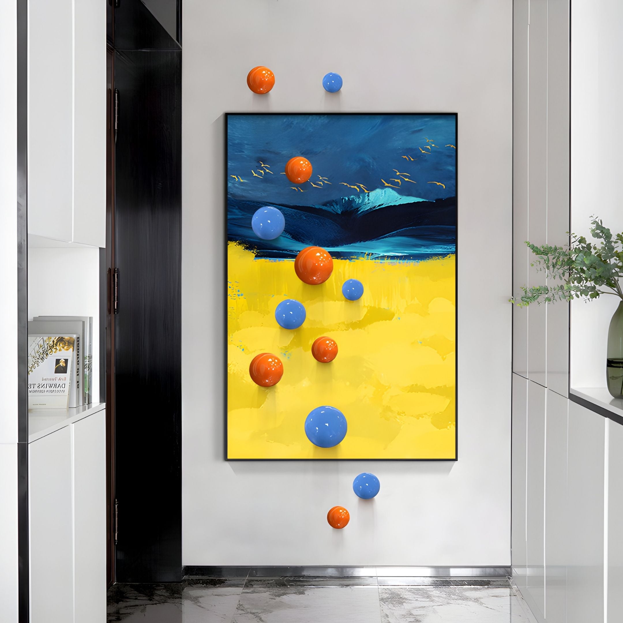 A hallway showcases Giant Sculptures' Aerisphere Mountain Glow Vertical 3D Wall Art With Metal Balls, featuring a vibrant landscape-inspired backdrop in yellow, blue, and dark hues with floating orange and blue metal spheres. White cabinets and a potted plant line the right.