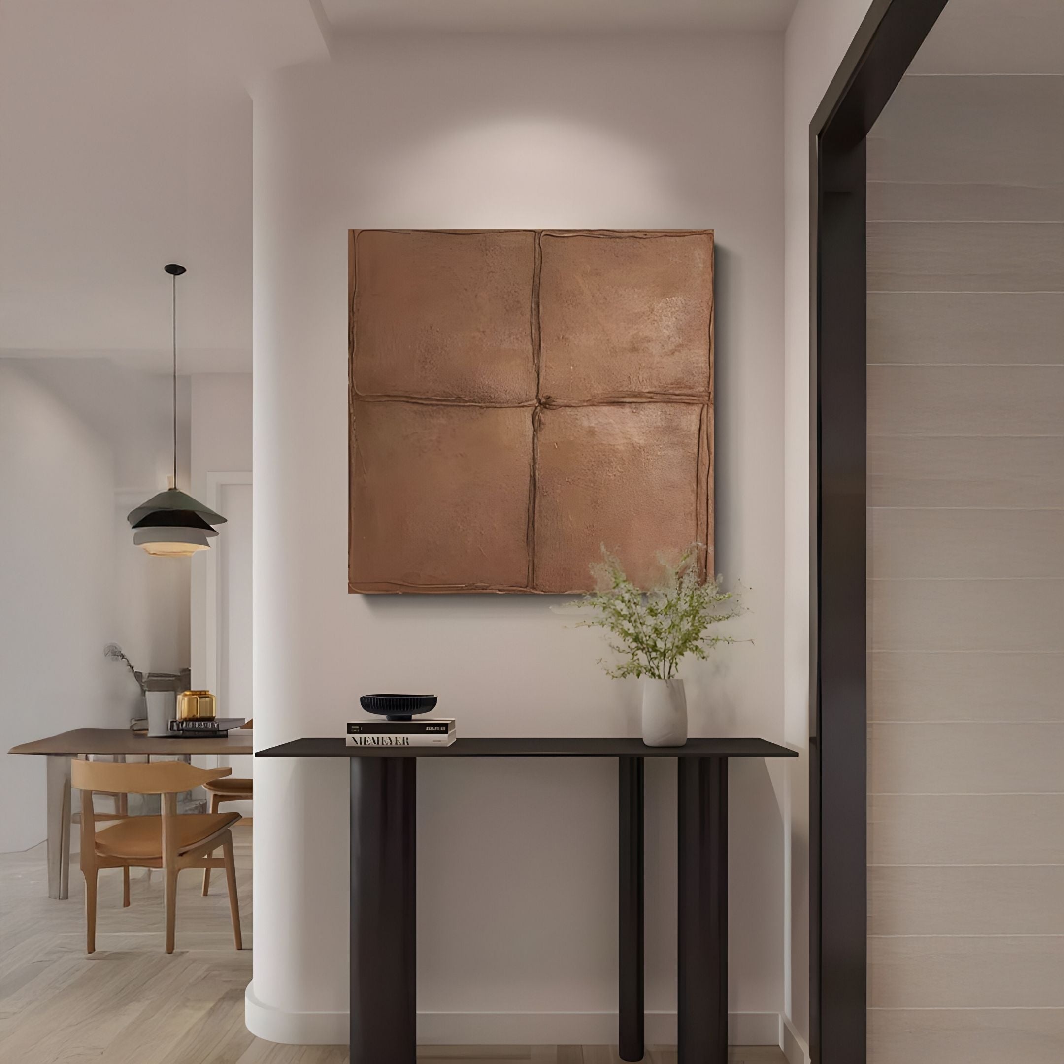 A modern entryway showcases a dark console with books and flowers, beneath the Giant Sculptures Terracrecta Cocoa Brown Painted Textured Square 3D Wall Art. In the background, a dining set sits under a hanging light.
