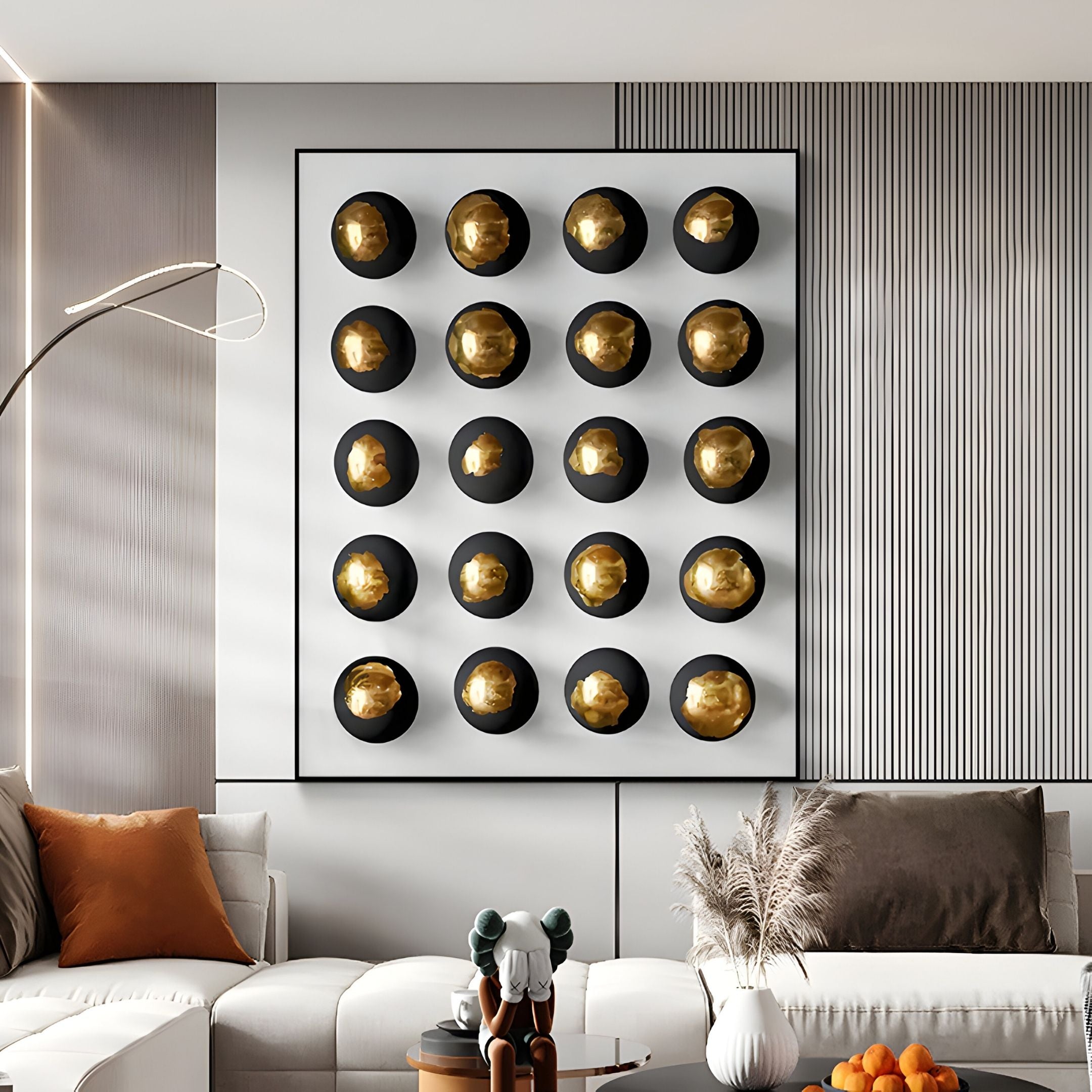 A modern living room showcases the Orbivelle Black-Gold Patch Sphere & White Panel 3D Wall Art by Giant Sculptures, paired with a white couch, brown and gray cushions, floor lamp, coffee table decor, and a bowl of oranges.