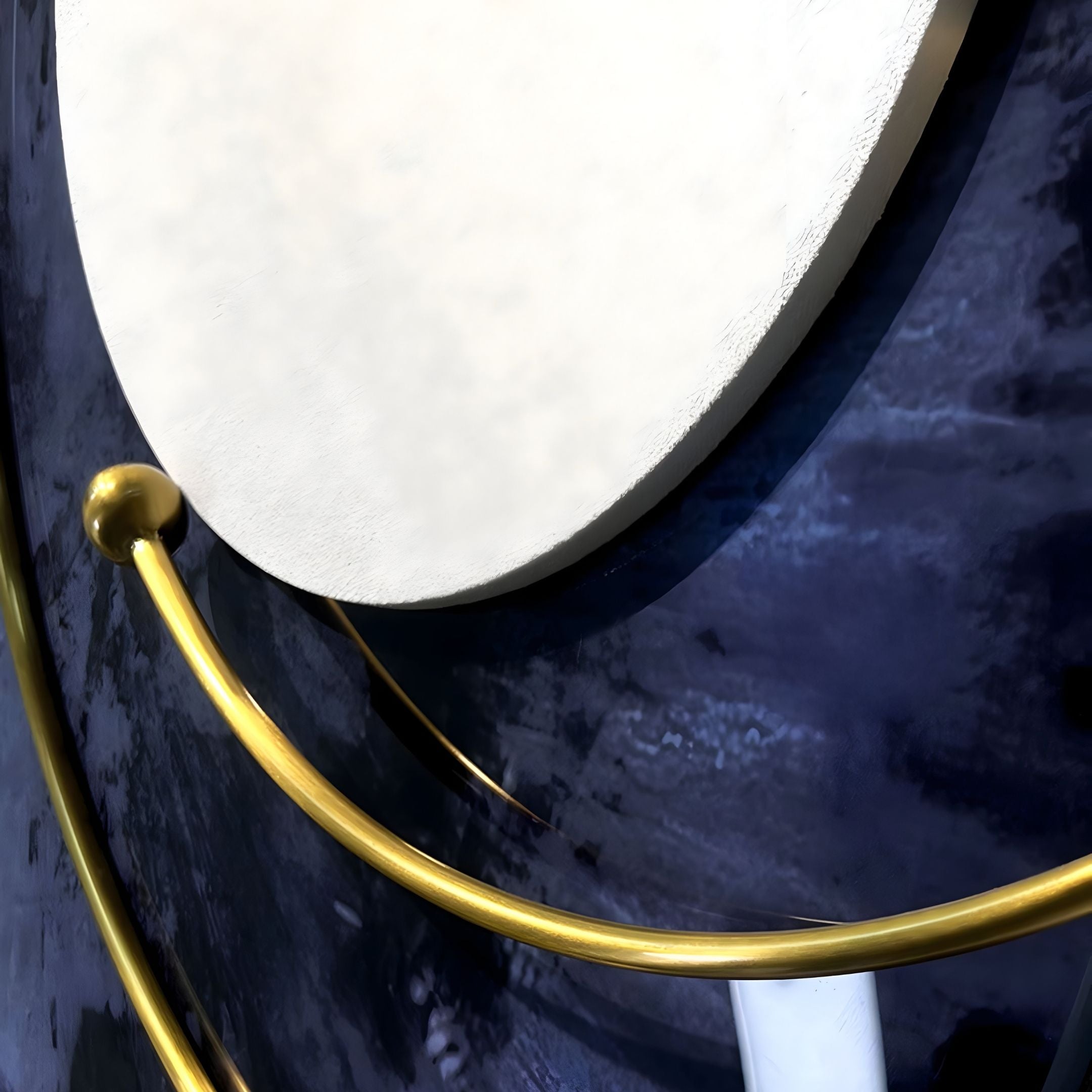 Close-up of Giant Sculptures’ Aurelios Sapphire Iris Crystal Porcelain & Gold Orbit 3D Wall Art, featuring a textured white circle on a dark blue background with smooth golden rods elegantly curving across the design.