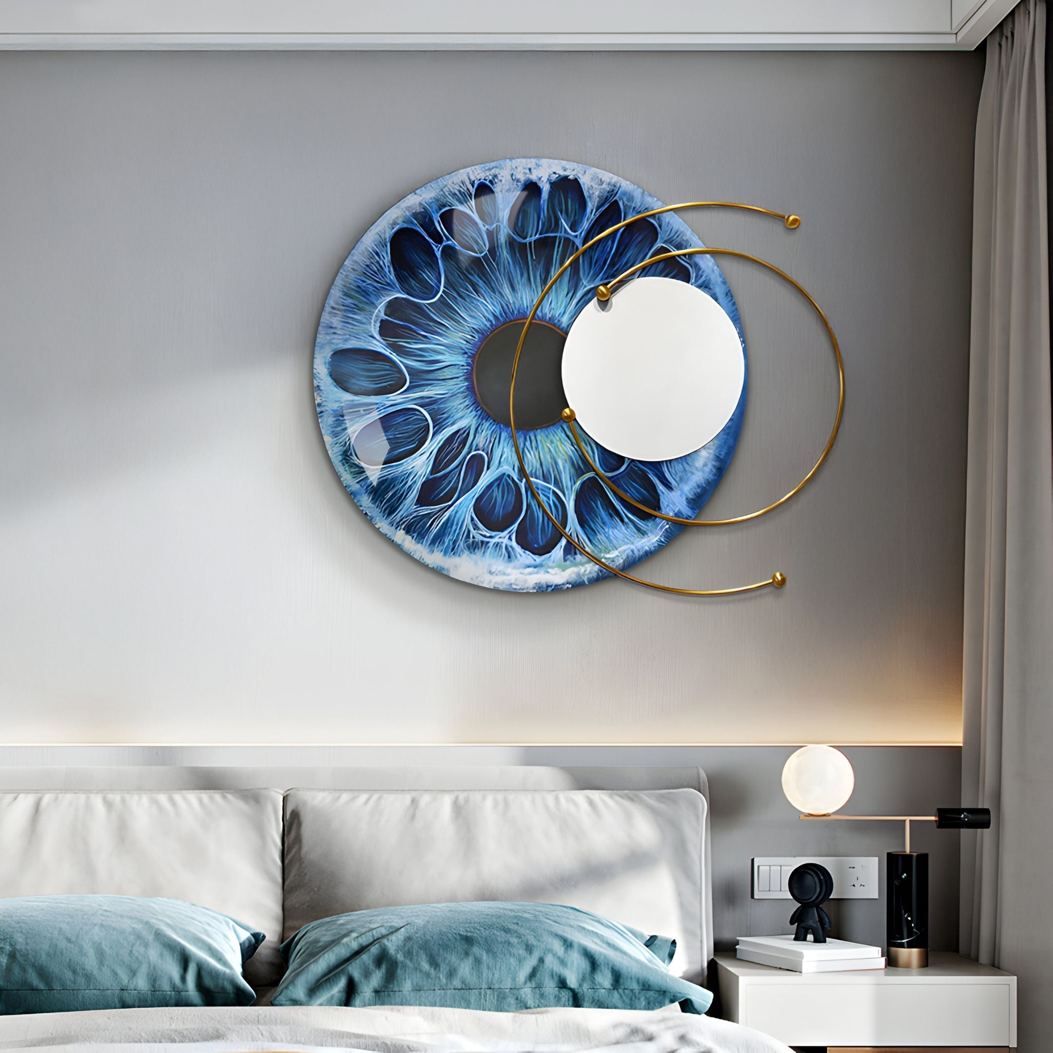 A modern bedroom showcases a bed with blue and white bedding beneath the Aurelios Oceanic Halo Crystal Porcelain & Gold Orbit 3D Wall Art by Giant Sculptures, featuring blue patterns, gold arcs, and a round mirror. A nightstand displays a lamp and decor.