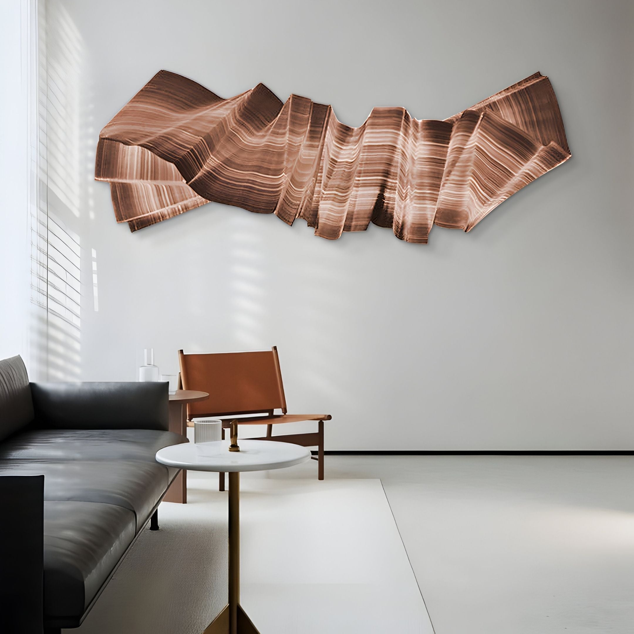 A modern living room with a gray sofa, brown leather chair, white round coffee table, and Giant Sculptures' Vellun Wave Copper Flow Sculptural 3D Wall Art on a light wall. Sunlight through blinds casts soft shadows, highlighting the contemporary style.