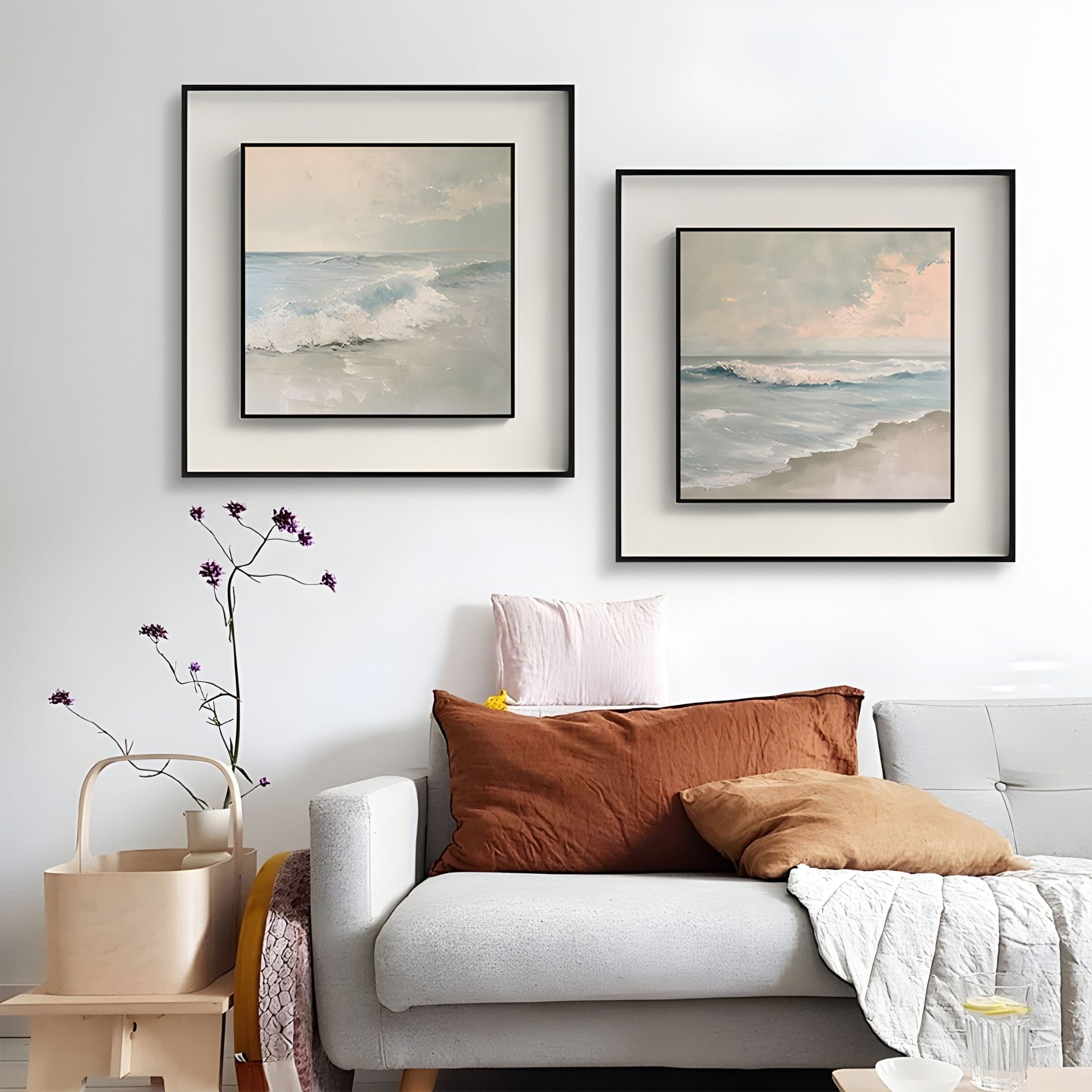 A modern living room with a light gray sofa, brown and pink cushions, a beige quilt, a basket of flowers, and Giant Sculptures' Tidalume III Soft Dawn Shoreline Double Framed Wall Art hanging on a white wall.