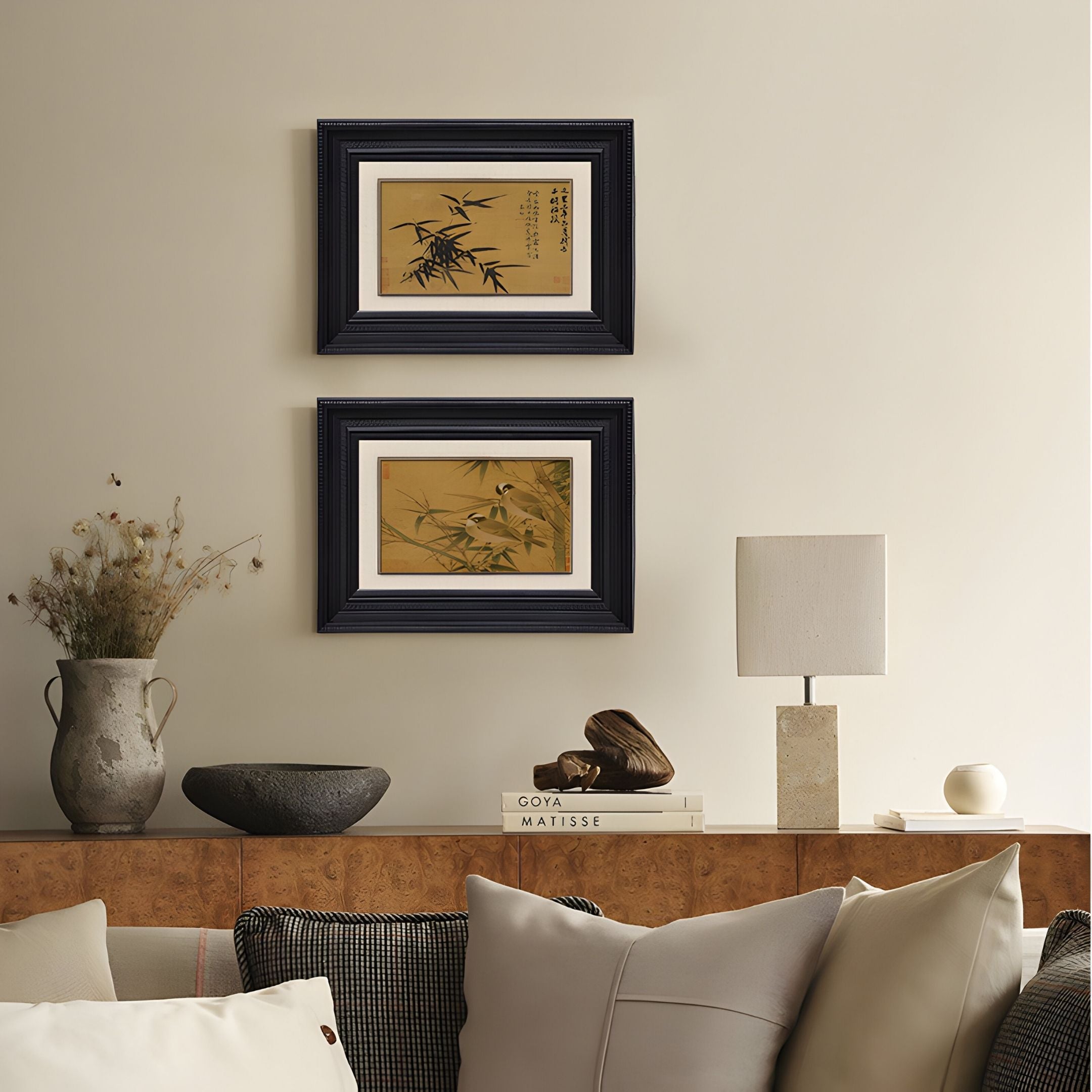 A cozy living room with beige walls, neutral pillows on a sofa, a table lamp, dried flowers in a vase, and Giant Sculptures' Kansora Bamboo Brushwork Classic 2-Set Framed Wall Art hanging above a wooden console.