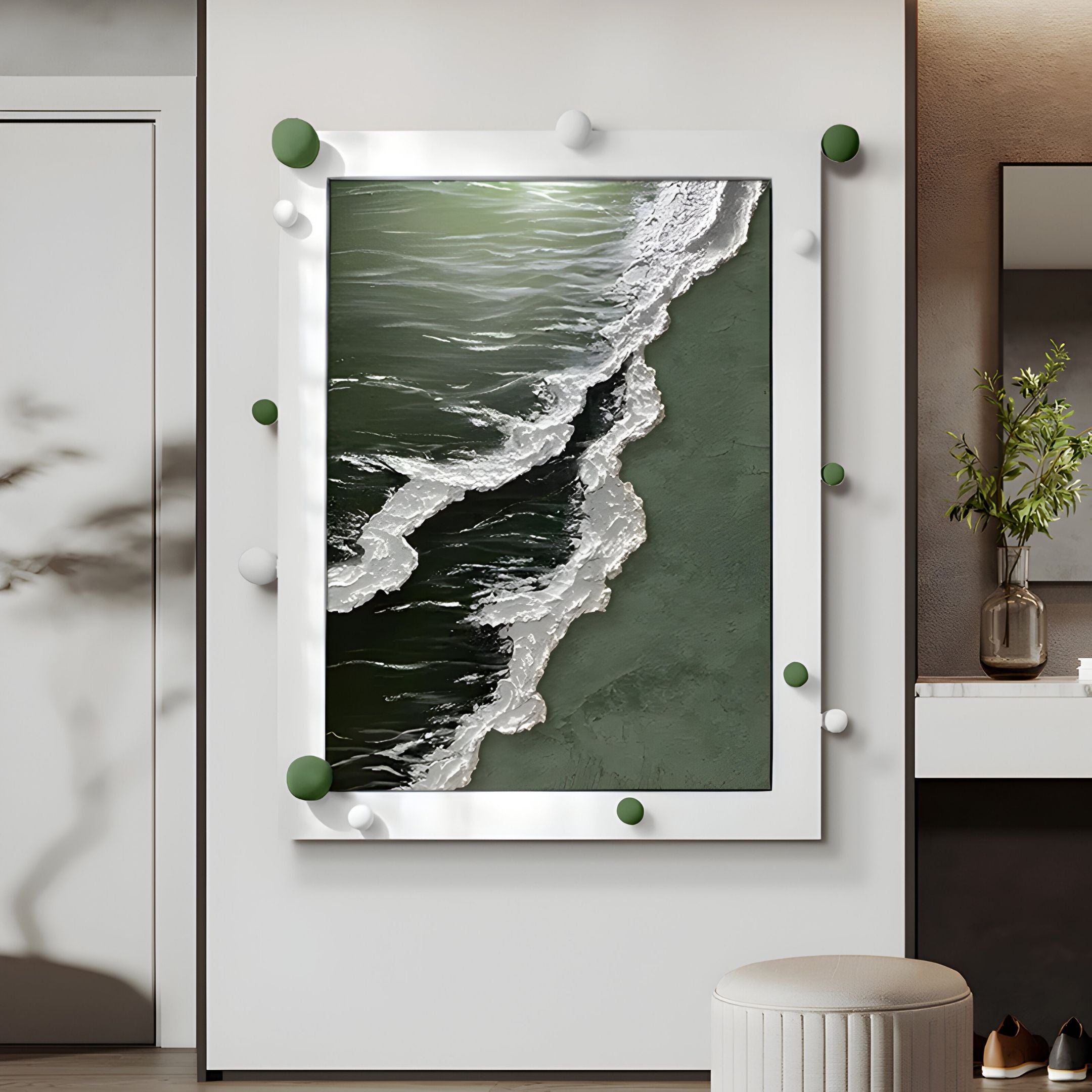 The Vivexa Green Shoreline Textured Ocean Abstract 3D Wall Art by Giant Sculptures, featuring ocean waves and green-white spheres in a white frame, hangs on a white wall near a small plant, counter, and stool.