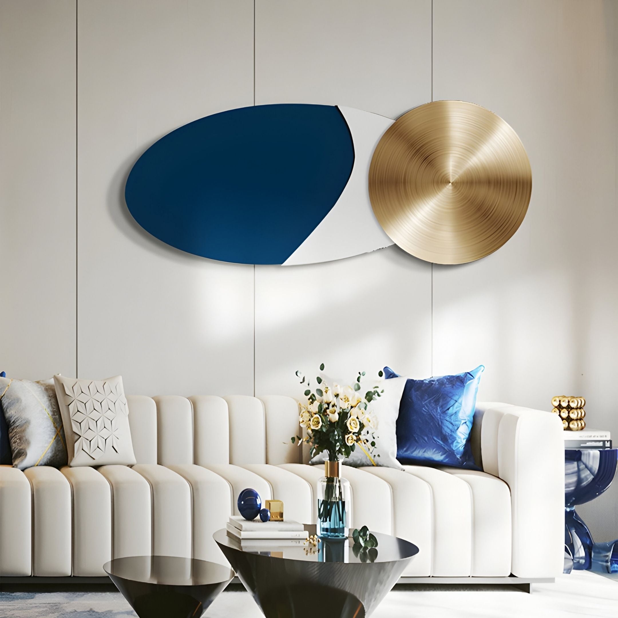 A modern living room featuring a white sofa, blue and white pillows, flowers in a glass vase, and contemporary décor styled with the Aurelune Navy & White Gold Metal Disc 3D Wall Art by Giant Sculptures above the sofa.