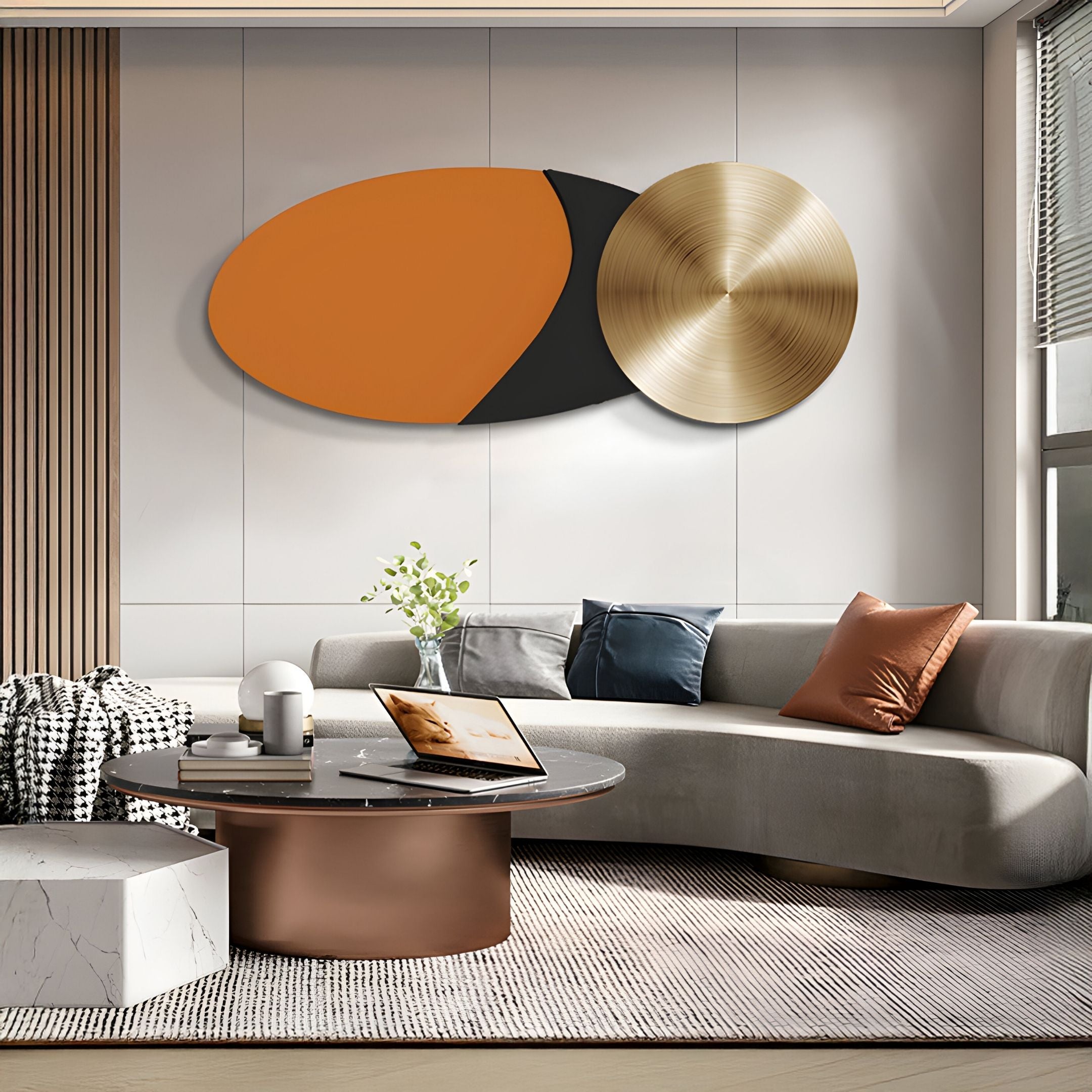 A modern living room with a curved beige sofa, round coffee table, pillows, and a laptop. Above the sofa hangs Giant Sculptures' Aurelune Amber & Black Gold Metal Disc 3D Wall Art as sunlight streams through a large window.