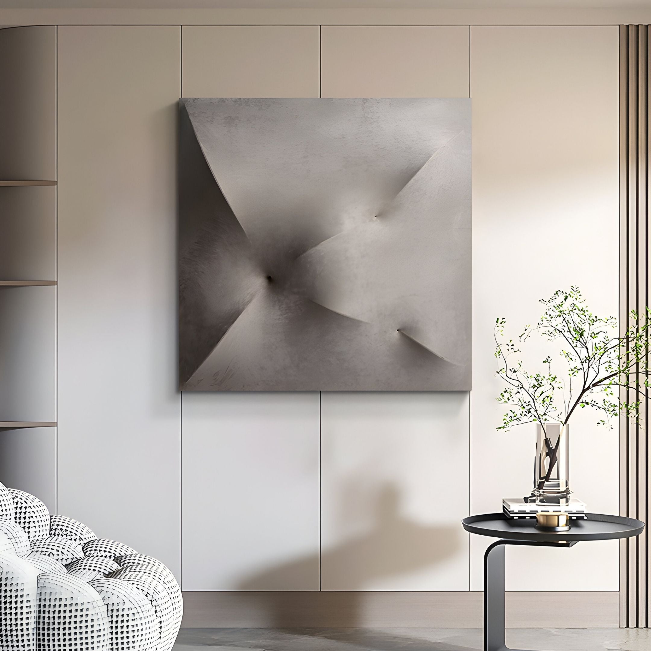 A minimalist room with light walls showcases Giant Sculptures’ Veylora Stone Grey Folded Texture Fabric 3D Wall Art. A modern round table with a plant and books stands next to a textured white chair.