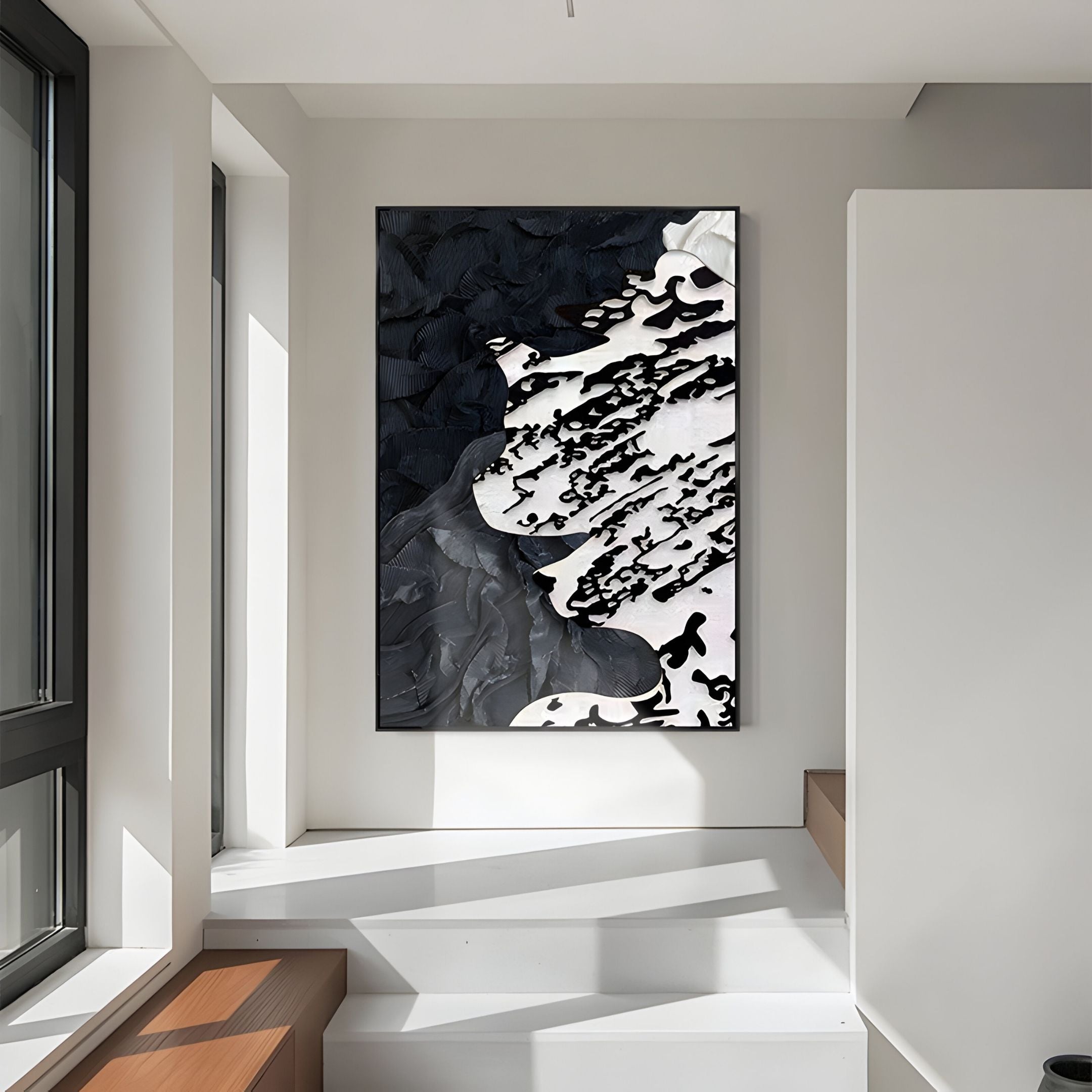 The Nivoria I Black & White Textured Abstract 3D Wall Art by Giant Sculptures features bold patterns and hangs on a white wall in a modern, sunlit room with large windows and wooden steps.