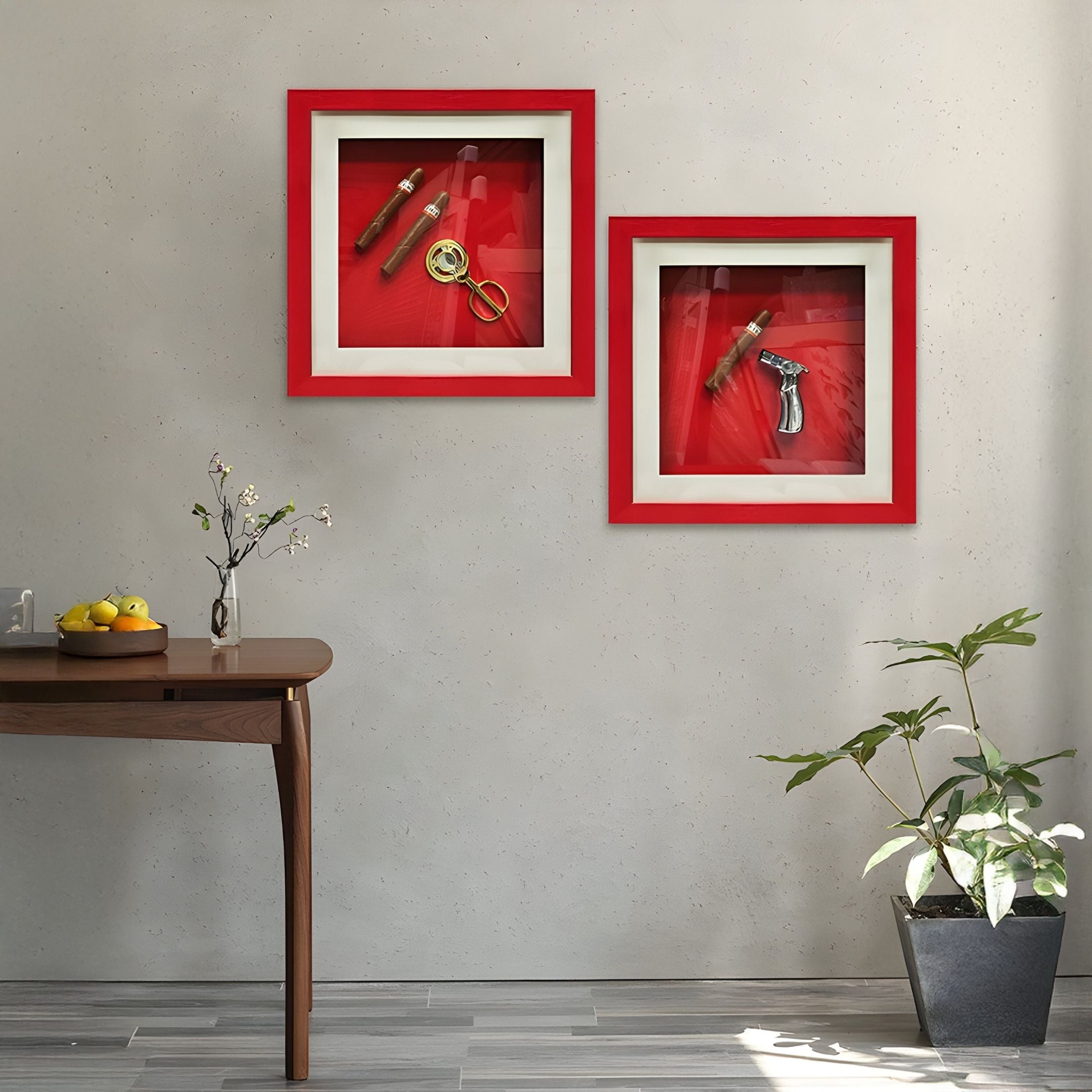 A modern interior showcases the Cavendro Single Cigar & Torch Lighter Framed Wall Art by Giant Sculptures—two red-framed pieces on a beige wall. Nearby, a wooden table holds fruit and a plant, with a potted plant placed on the floor.