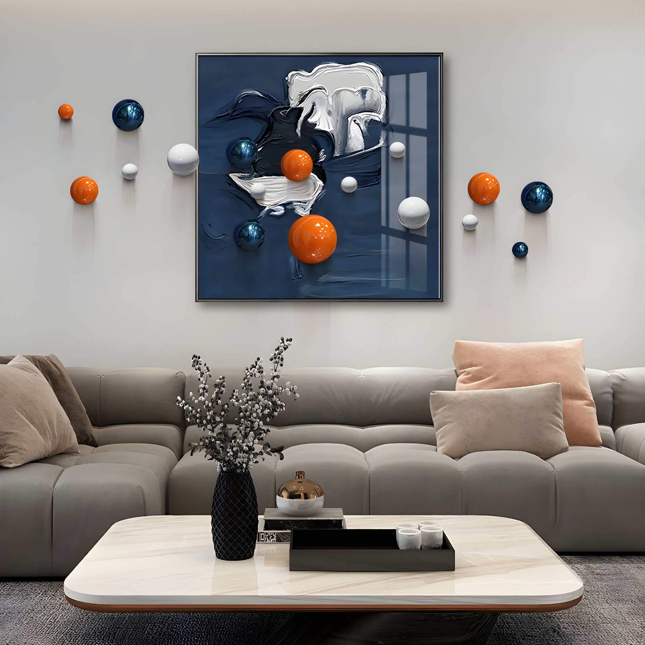 A modern living room with a gray sectional, peach pillows, marble coffee table, and the Aeroluxe Midnight Blue Abstract 3D Wall Art With Metal Balls by Giant Sculptures—featuring blue, orange, and white spheres above the sofa.