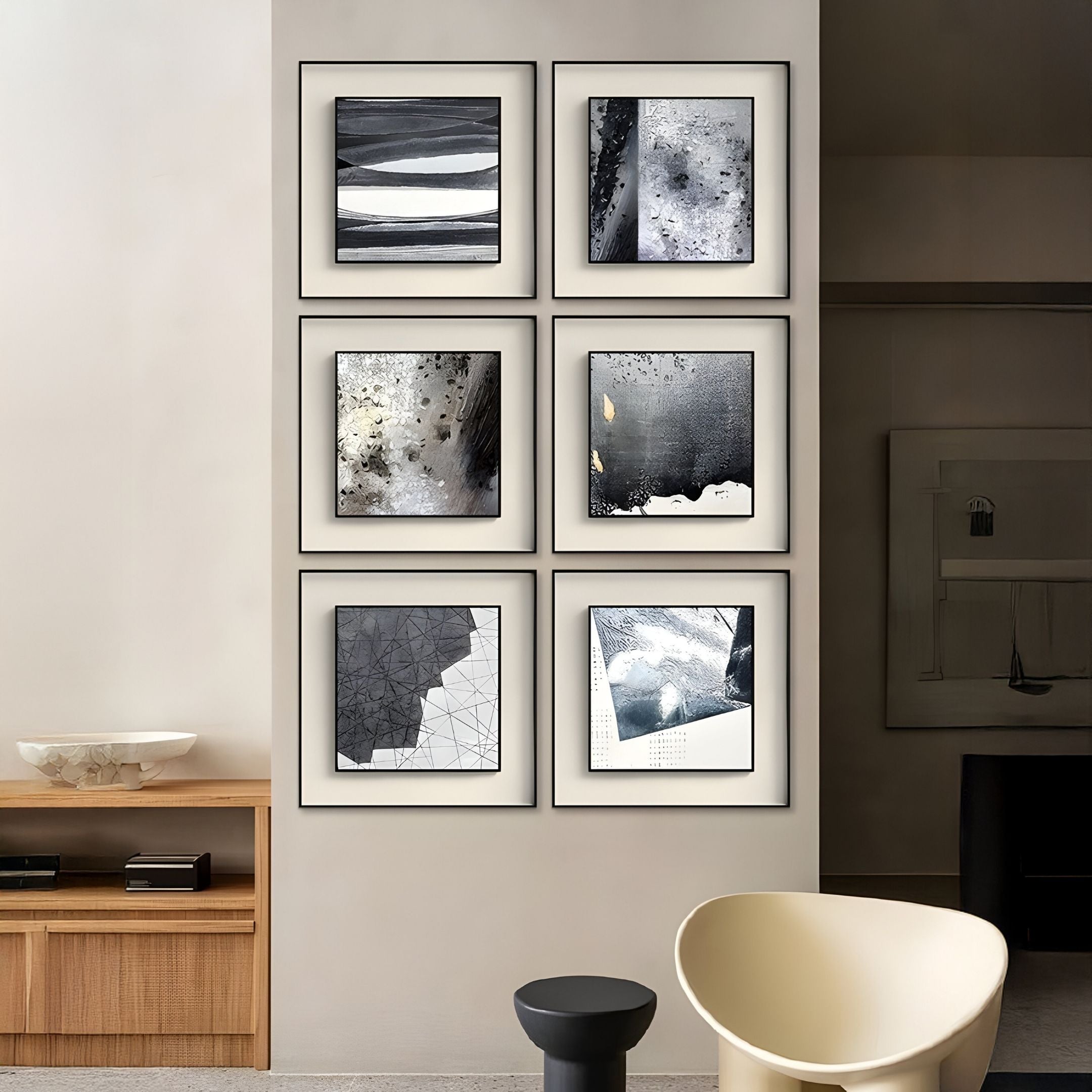 Six Stratonis Monochrome Layered Textured Framed Wall Art pieces by Giant Sculptures are displayed in two columns above minimalist wooden furniture, complemented by a cream chair and small black side table in a modern living space.