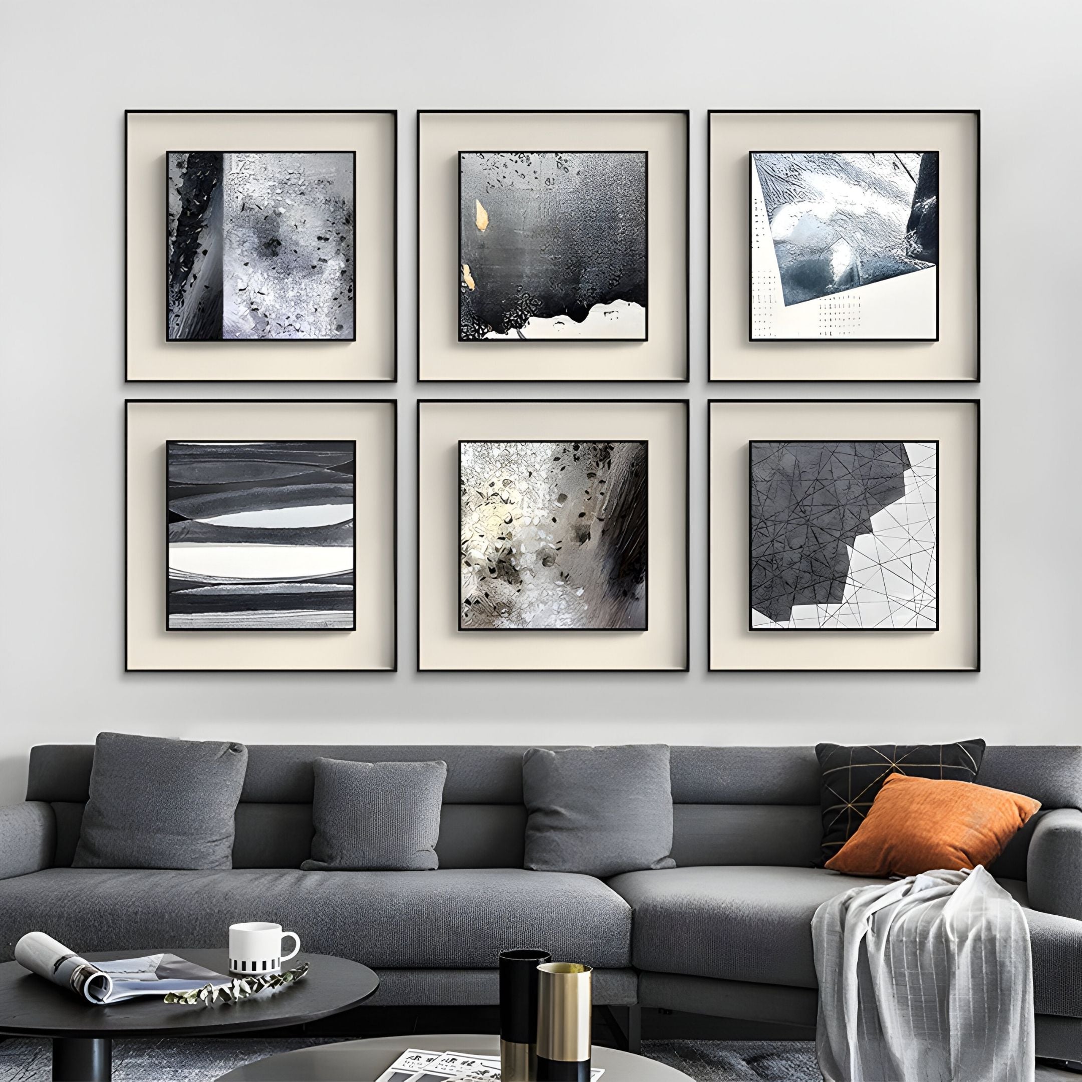 A modern living room with a gray sectional sofa, orange and black cushions, a round coffee table, and six Stratonis Grey Terrain Textured Framed Wall Art pieces by Giant Sculptures arranged above the sofa.