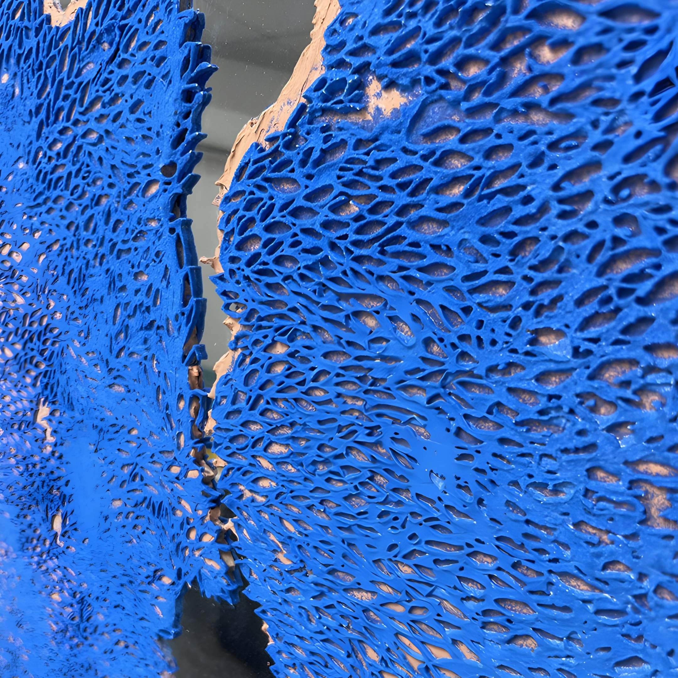 Close-up of Cerulex Blue Rift Textured Steel Mirror 3D Wall Art by Giant Sculptures, featuring a bright blue net-like textured pattern with organic holes on a tan and dark steel background for dramatic visual depth.