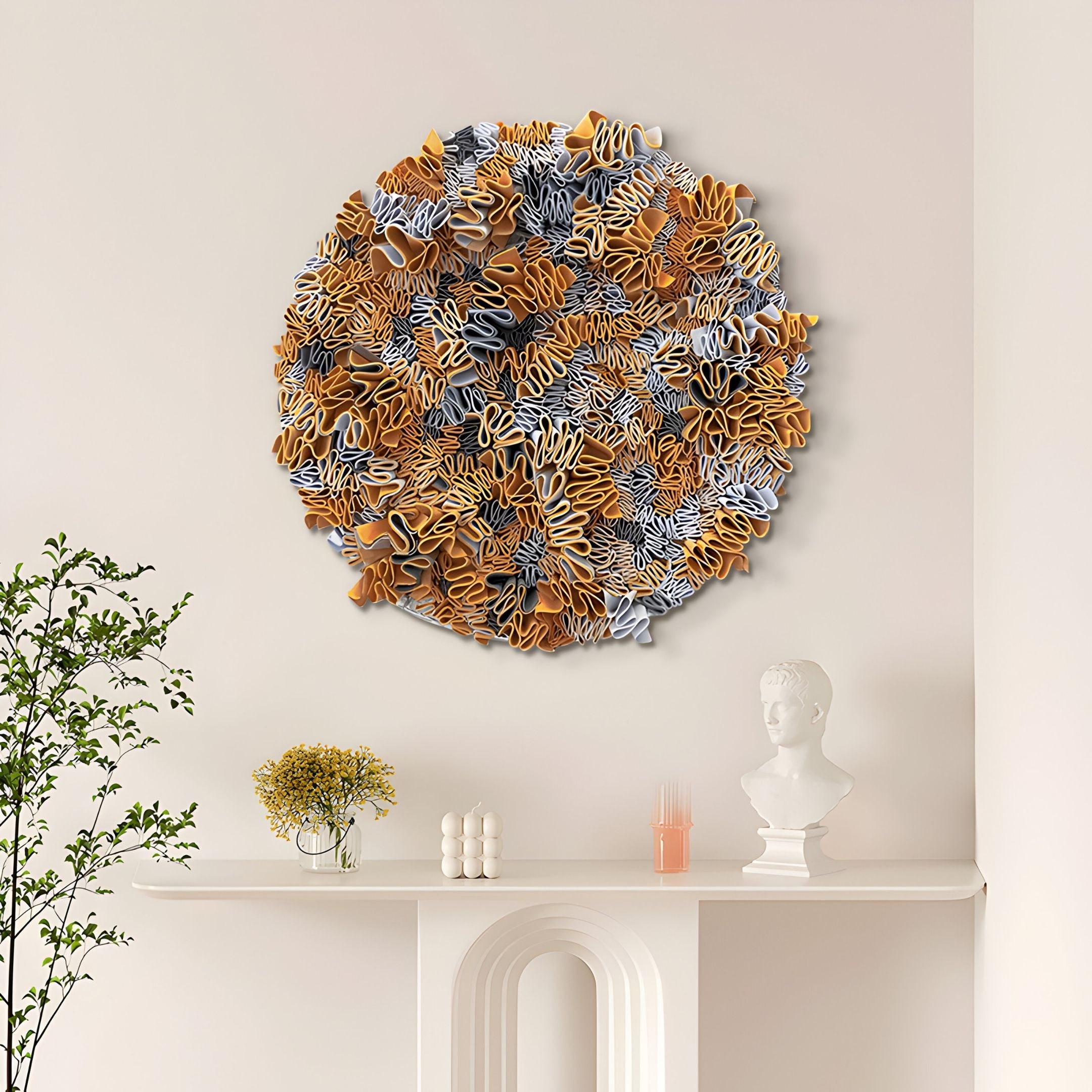 The Rivora Amber Ribbon Leather Circular 3D Wall Art by Giant Sculptures, with layered gold, white, and gray abstract shapes, hangs above a white mantel displaying a bust, candles, and a small yellow floral arrangement.