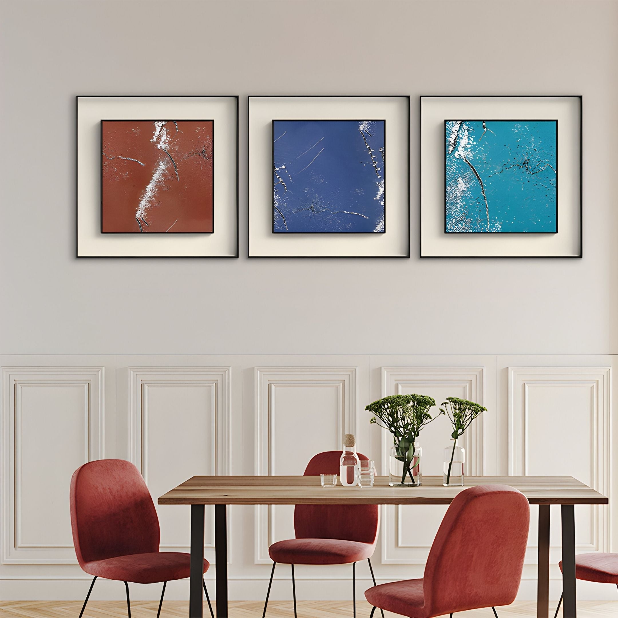 A modern dining room features a wooden table, red velvet chairs, and the Trevasse Copper Textured Abstract Framed Wall Art by Giant Sculptures in red, blue, and teal above. Glass bottles and vases with flowers complete the stylish look.