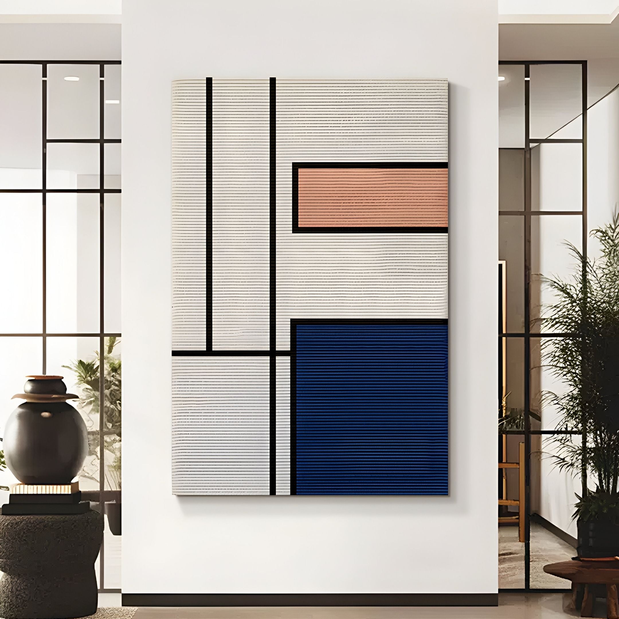 The Gridoria Peach & Navy Linear Block Woven Wall Art by Giant Sculptures features black lines dividing textured white, peach, and blue rectangles—ideal for modern decor in rooms with glass panels and potted plants.