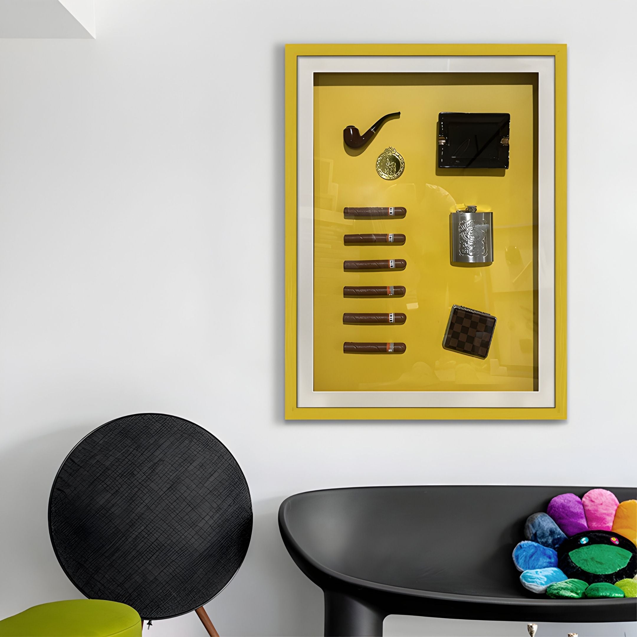 A modern room showcases the Gentaro Cigar & Gentleman Collectible Display Wall Art by Giant Sculptures—a yellow-framed shadow box of gentleman's items. Below, a black chair, table, and plush pillow complete this vintage smoking lounge decor.