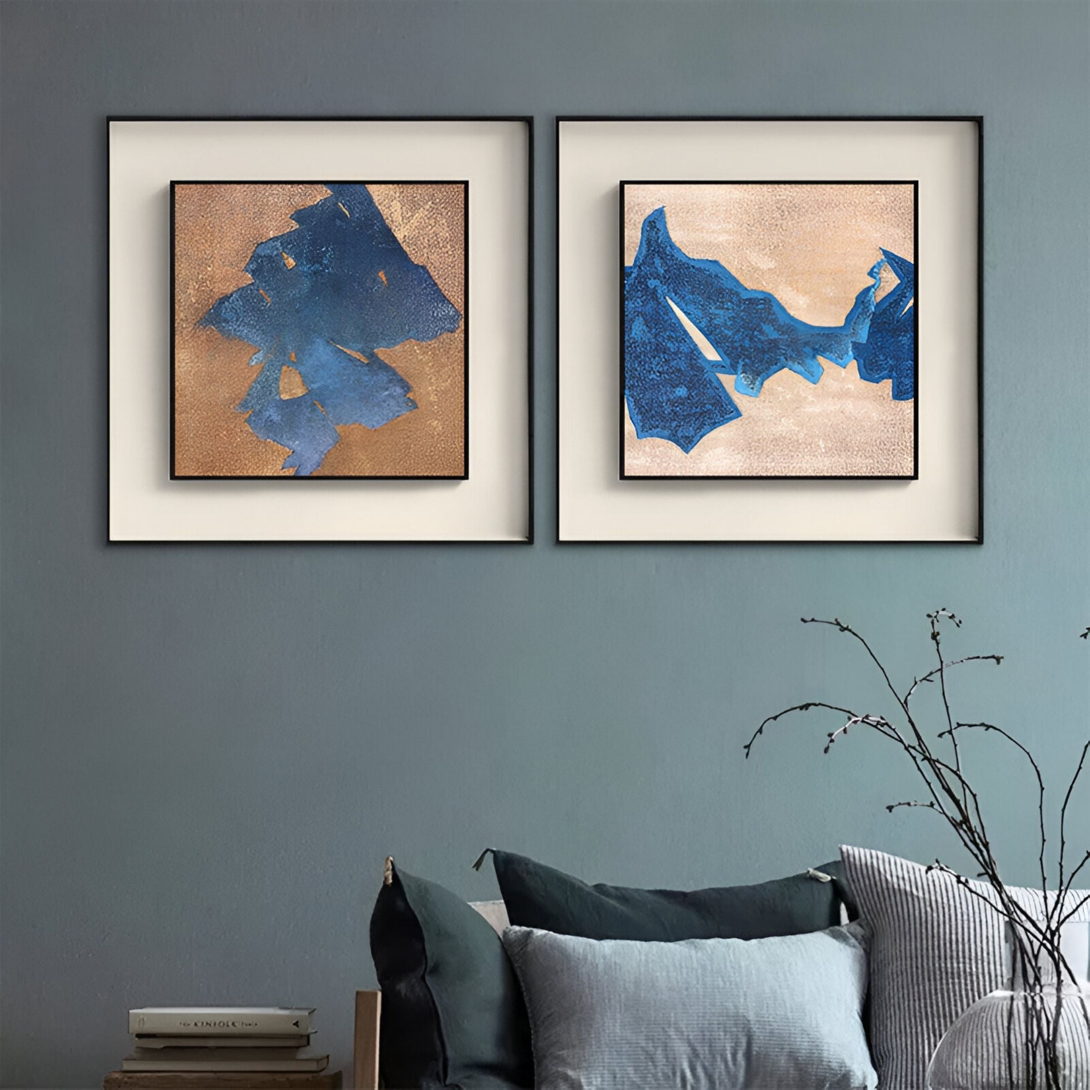 Stratum Indigo Drift Textured Abstract Framed Wall Art by Giant Sculptures hangs above a sofa with blue and gray cushions, elevating the room's contemporary style. A vase with bare branches and books rests on the nearby table.