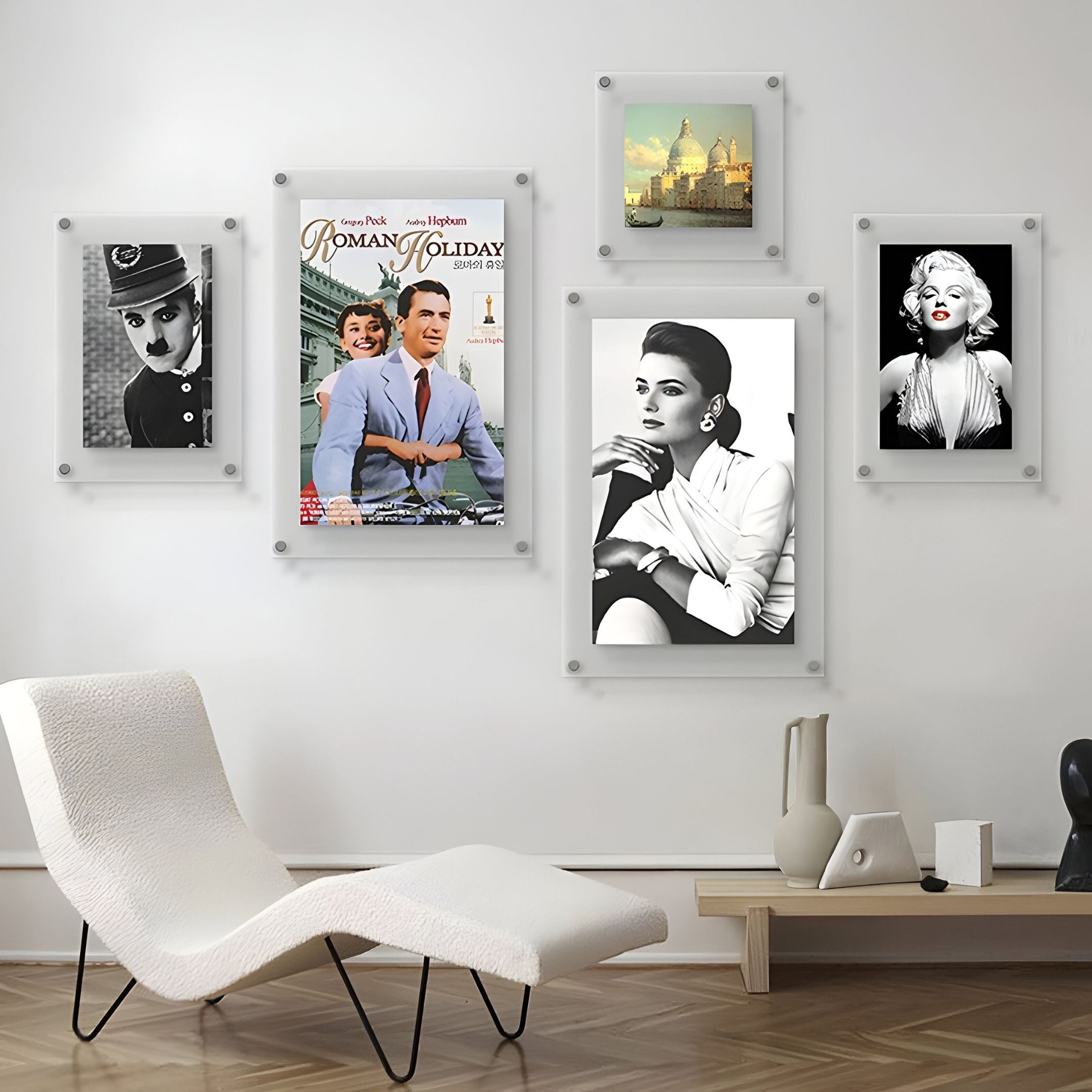 A modern living room showcases a white lounge chair and Giant Sculptures’ CineLuxe Classic Icons Retro 5-Panel Acrylic Wall Art, featuring film icons. Books, a lamp, and decor items rest on a low shelf.