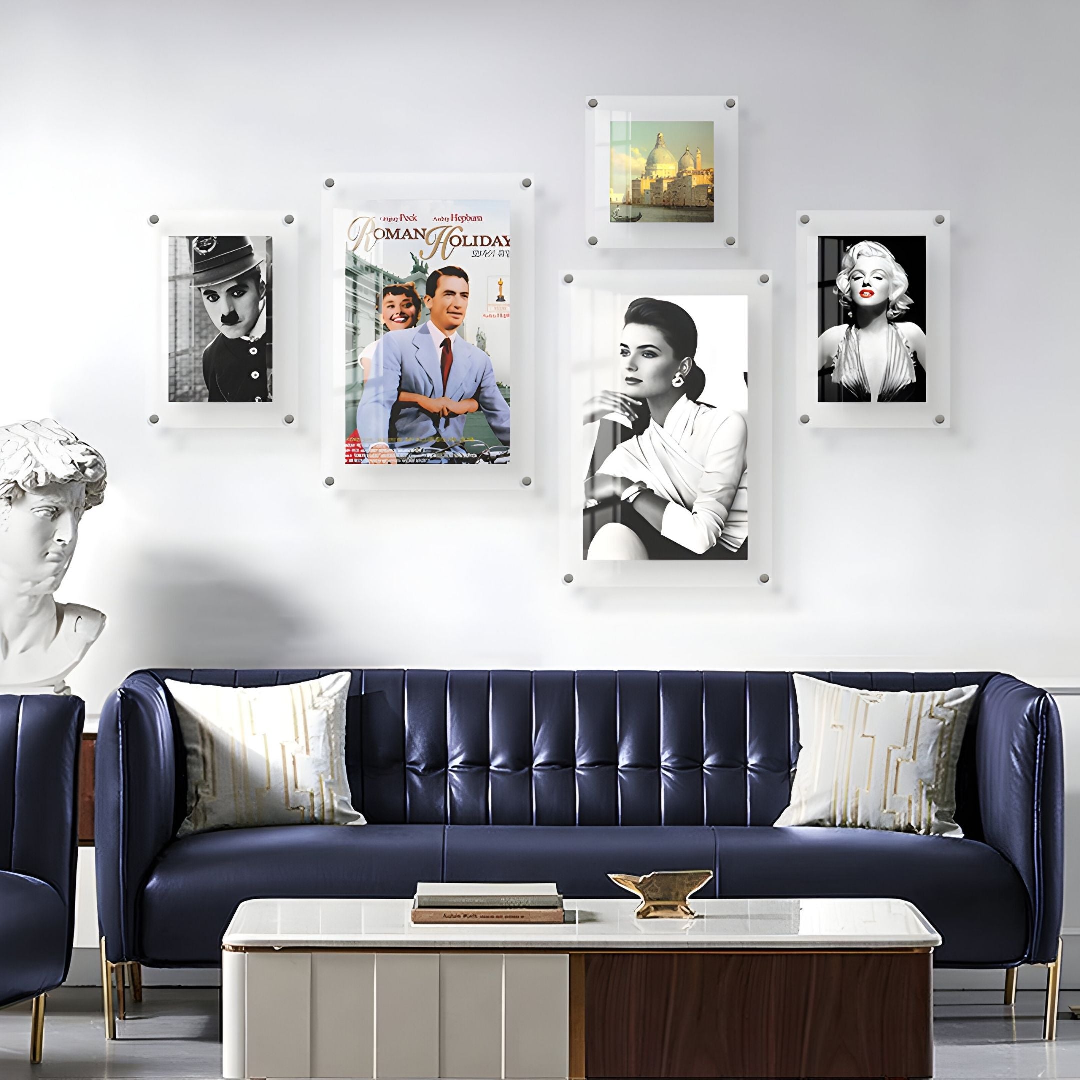 A modern living room with a dark blue sofa, white pillows, a white coffee table, a white sculpture bust, and the CineLuxe Classic Icons Retro 5-Panel Acrylic Wall Art by Giant Sculptures featured on the gallery wall.