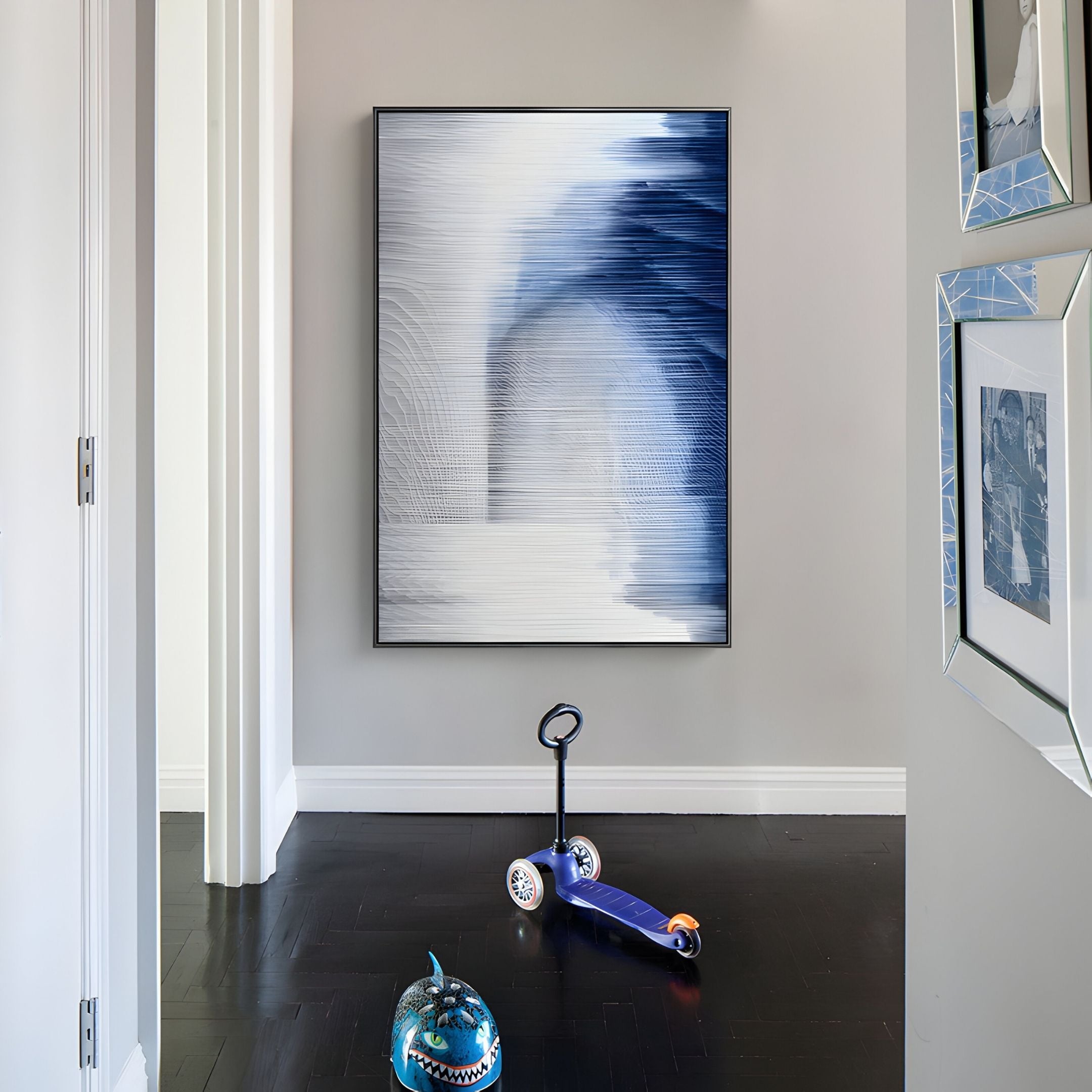 A hallway with dark wooden floors features the Striathen Cobalt & Grey Blur Textured Rope 3D Wall Art by Giant Sculptures, plus modern wall decor. A blue scooter and shark-shaped helmet sit on the floor; framed art appears on the right wall.