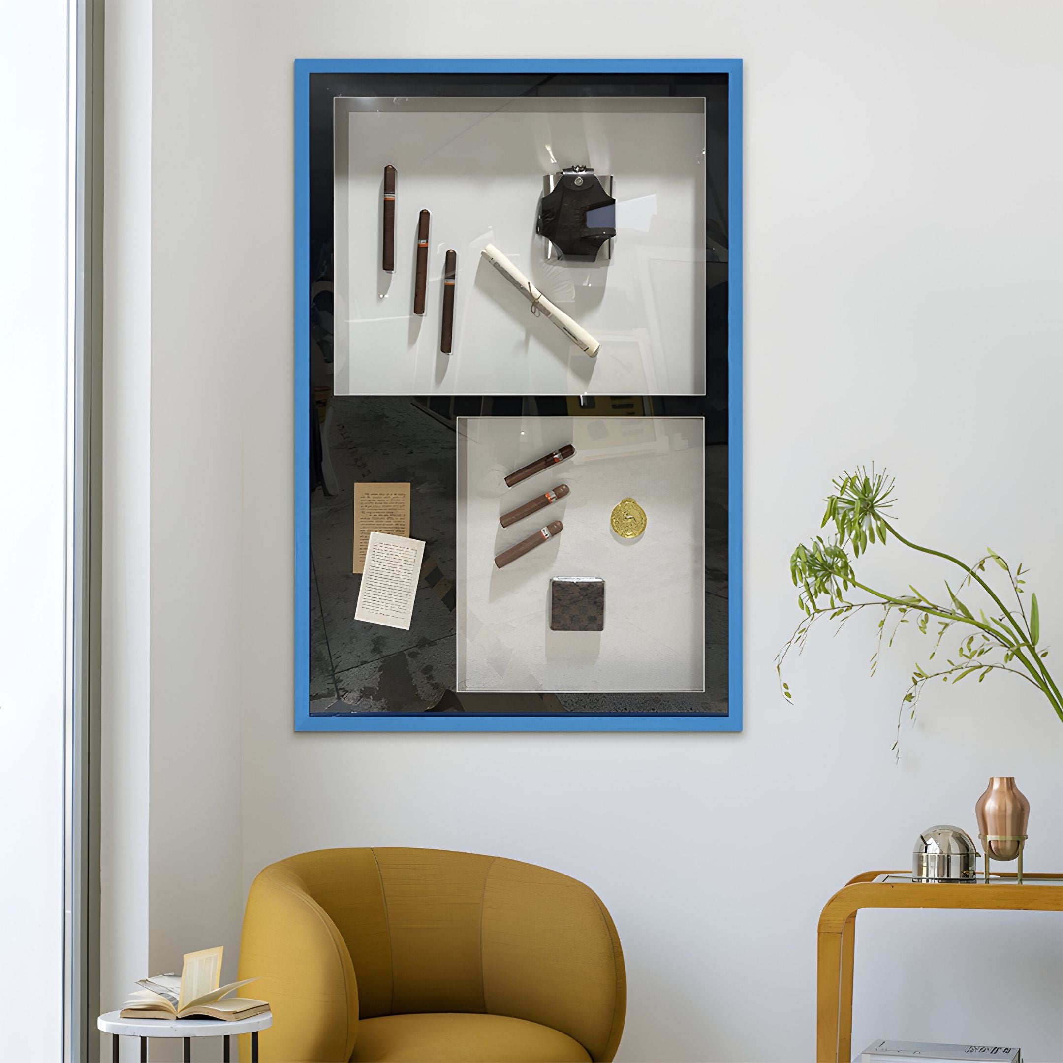 The Valet Noir Gentleman Cigar Gallery Box Framed Wall Art by Giant Sculptures features pens, a gold coin, cards, and cigar artwork—ideal gentleman decor for above a mustard-yellow chair and table with plant.