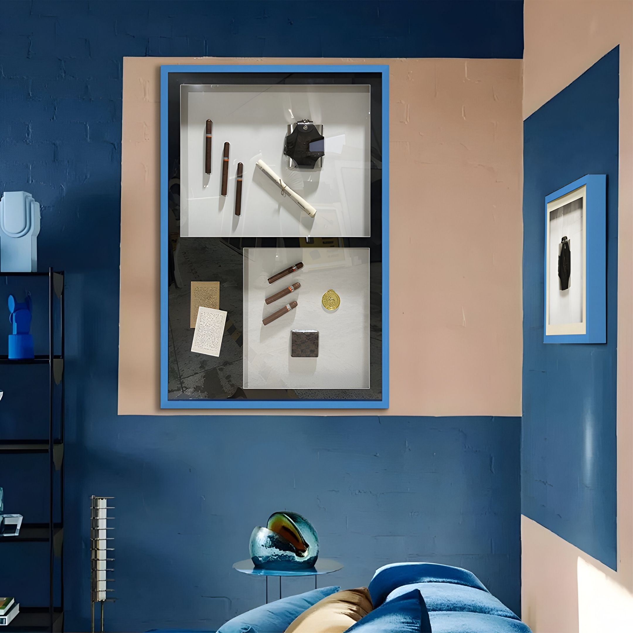 A modern room with blue and beige walls features Giant Sculptures' Valet Noir Gentleman Cigar Gallery Box Framed Wall Art, abstract framed pieces, a round blue glass decor, blue sofa, and shelves for a stylish contemporary touch.