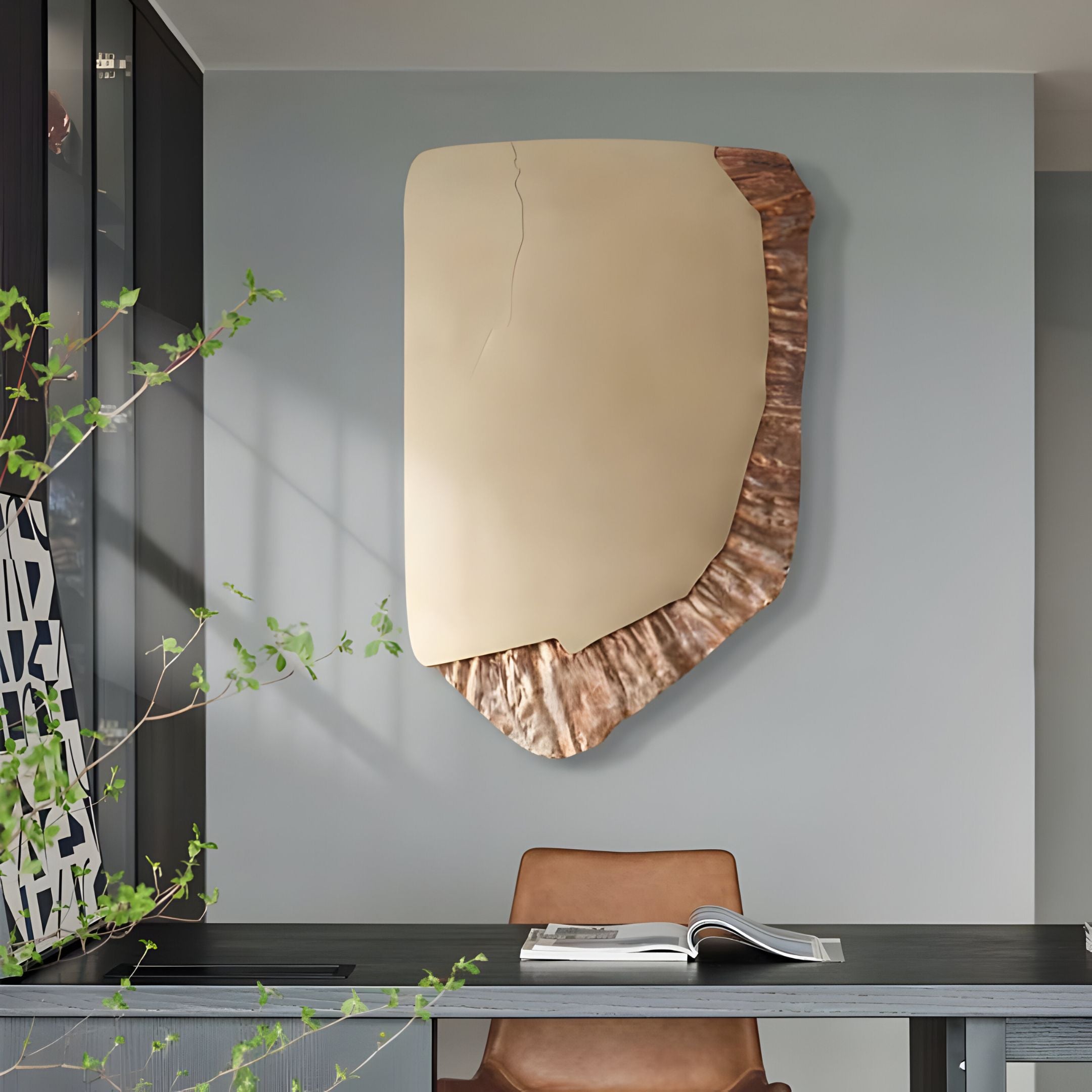 A modern office features a desk, brown leather chair, open book, and Giant Sculptures' Gildrift Gold Steel & Copper Ridge Textured 3D Wall Art with smooth beige and copper details on a light gray wall. A leafy plant sits in the foreground.