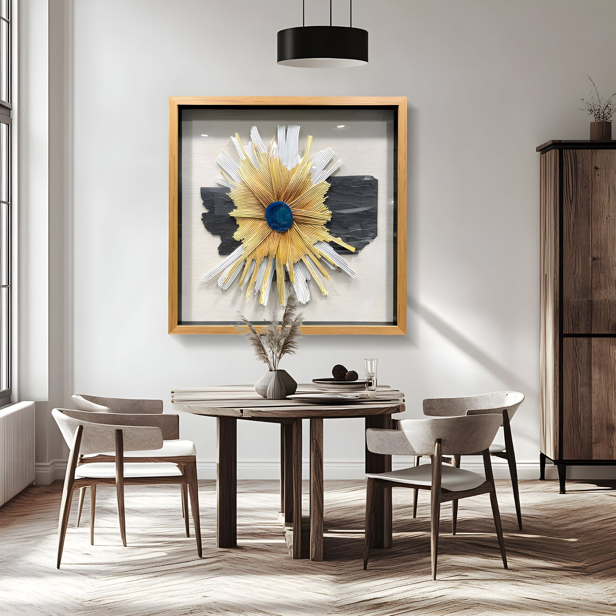 A modern dining area with a round wooden table, four beige chairs, a vase of dried flowers, and the Asterfold II White & Yellow Sunburst 3D Wall Art by Giant Sculptures in a wooden frame on a white wall. Natural light brightens the space.